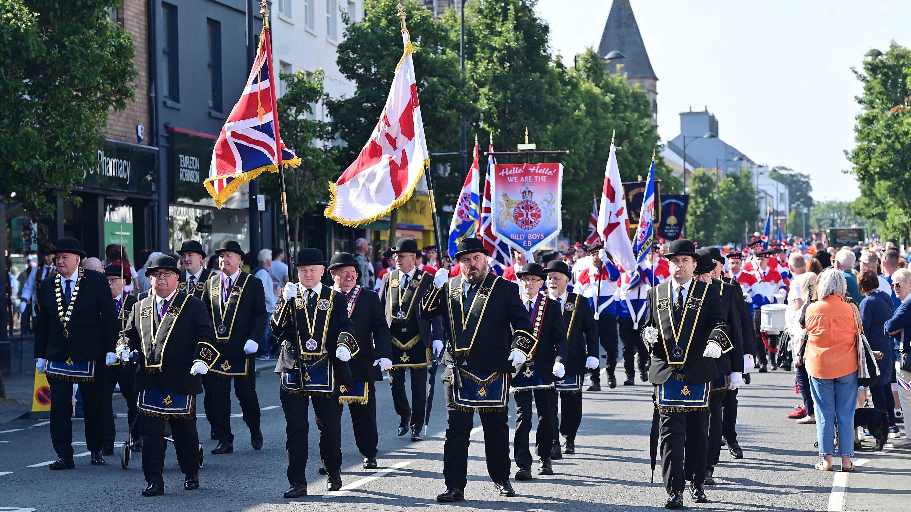 Members of the Royal Black Institution carrying flags and marching down a street in Holywood