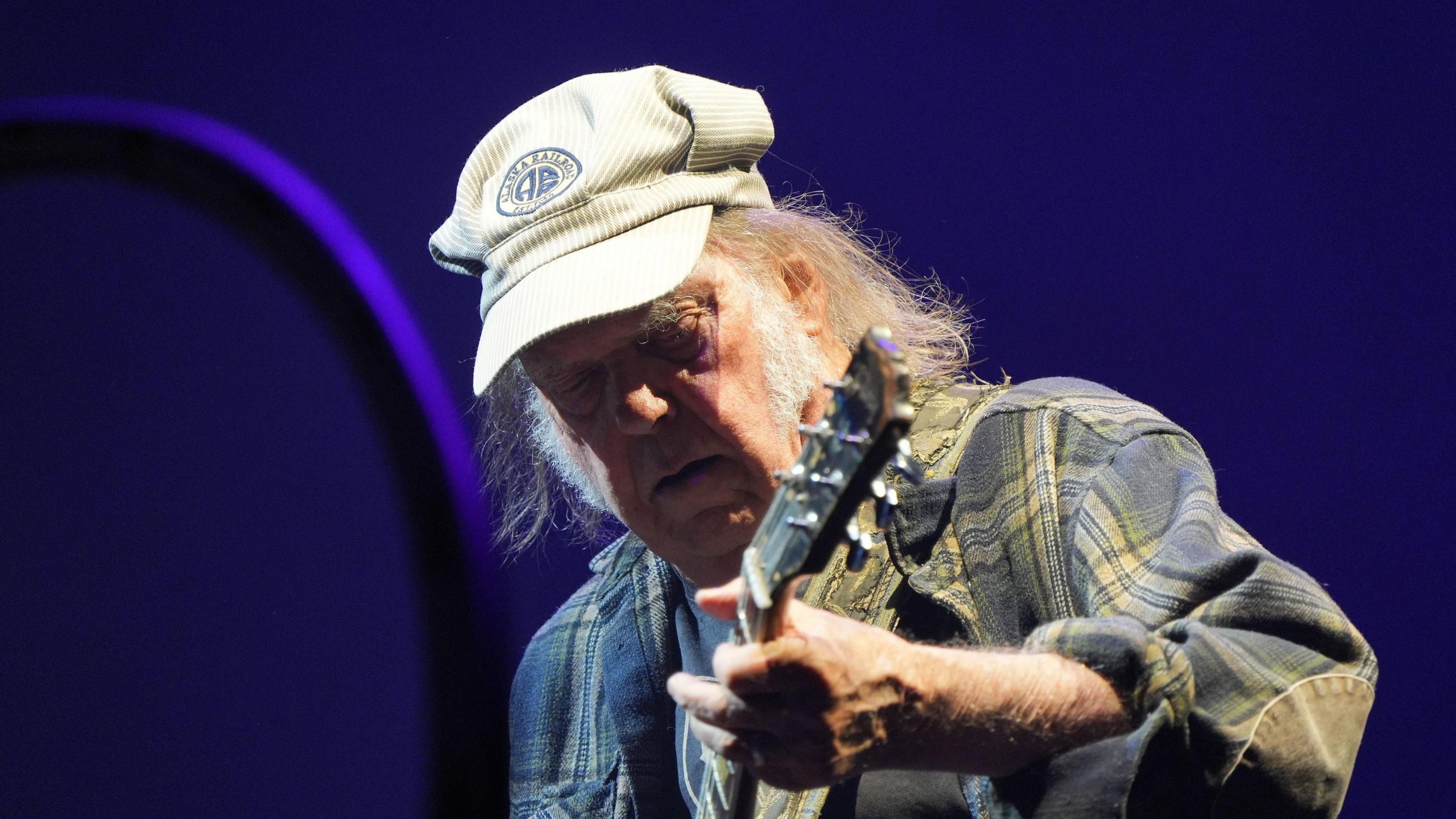 Neil Young performs in a plaid jacket and cap. 
