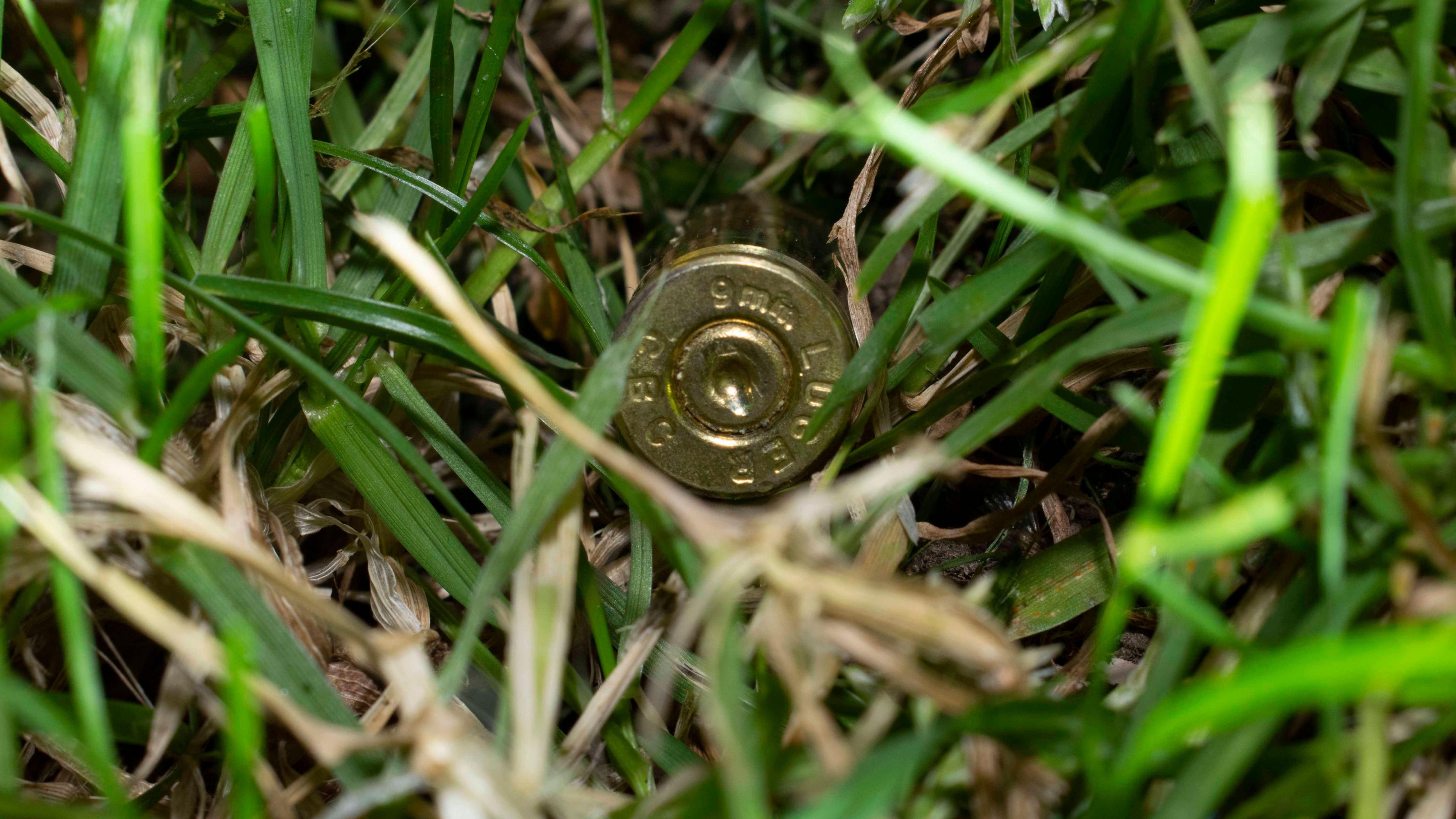 A golden bullet casing was found in the back garden of the property Paul Allen was living in when he was shot. It is surrounded by green and yellow grass.