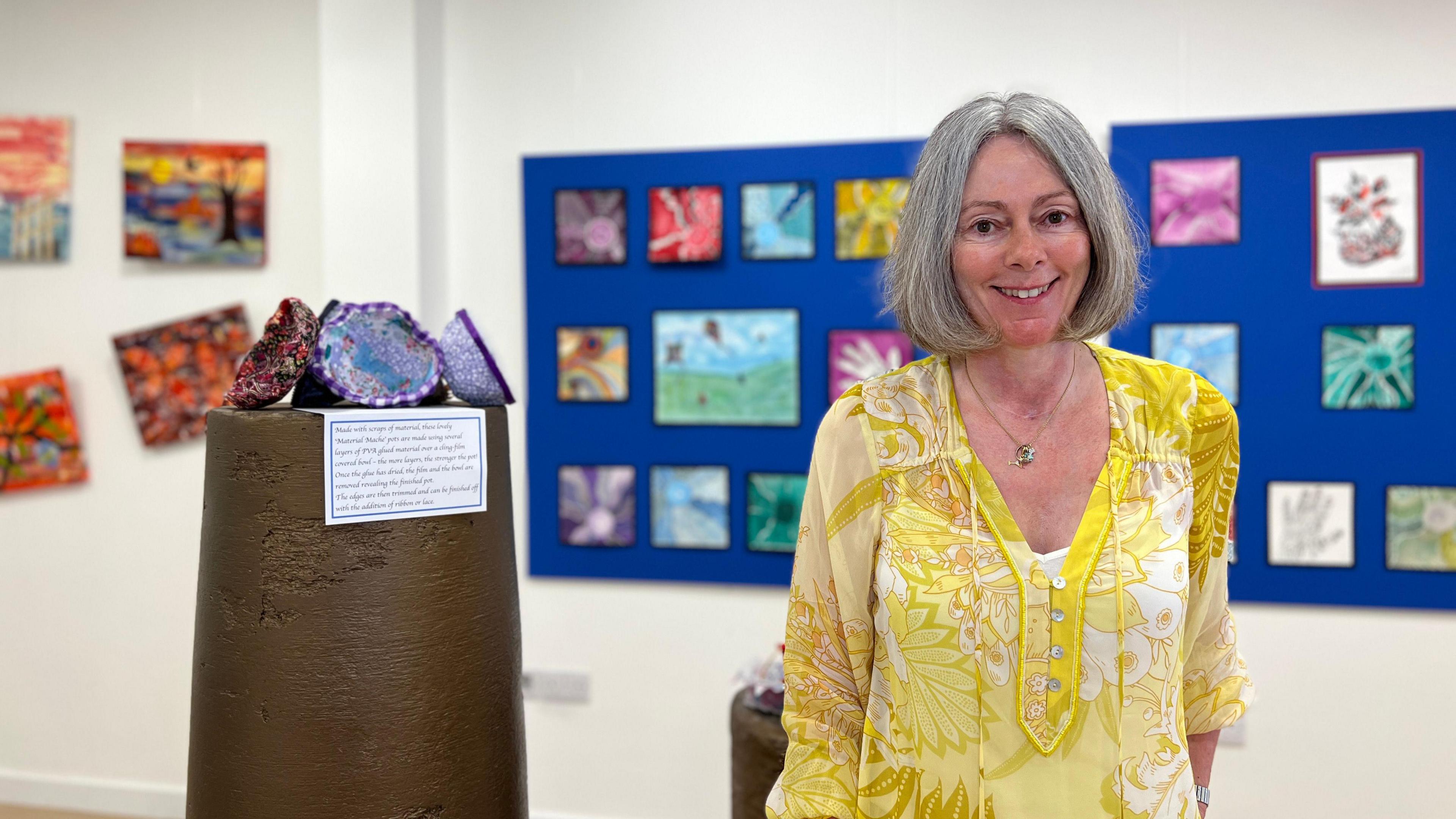 A woman in a yellow top stands in an art gallery