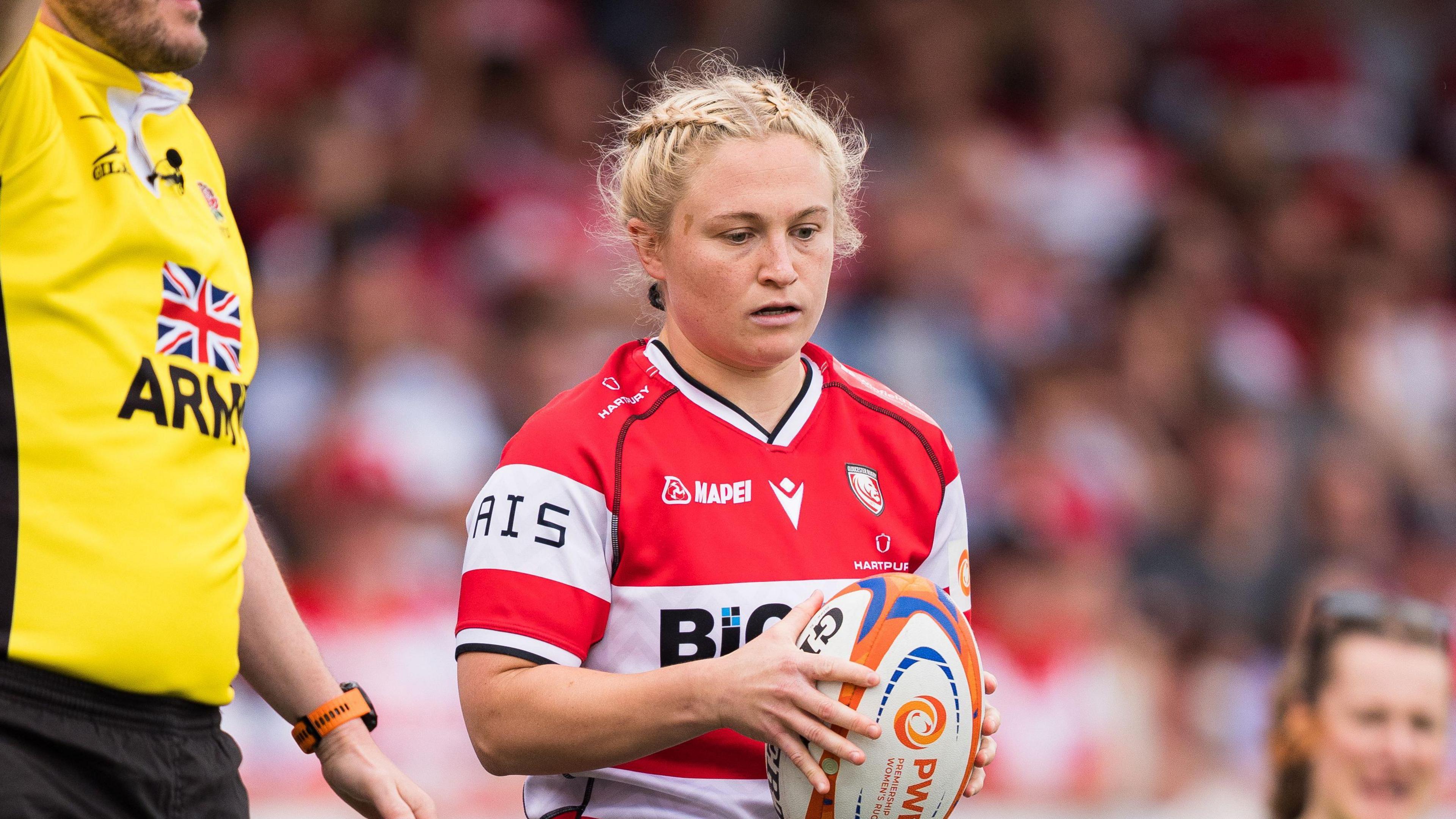 Neve Jones looks to the floor and holds a rugby ball between two hands as she stands on the side of the pitch preparing to throw a line-out
