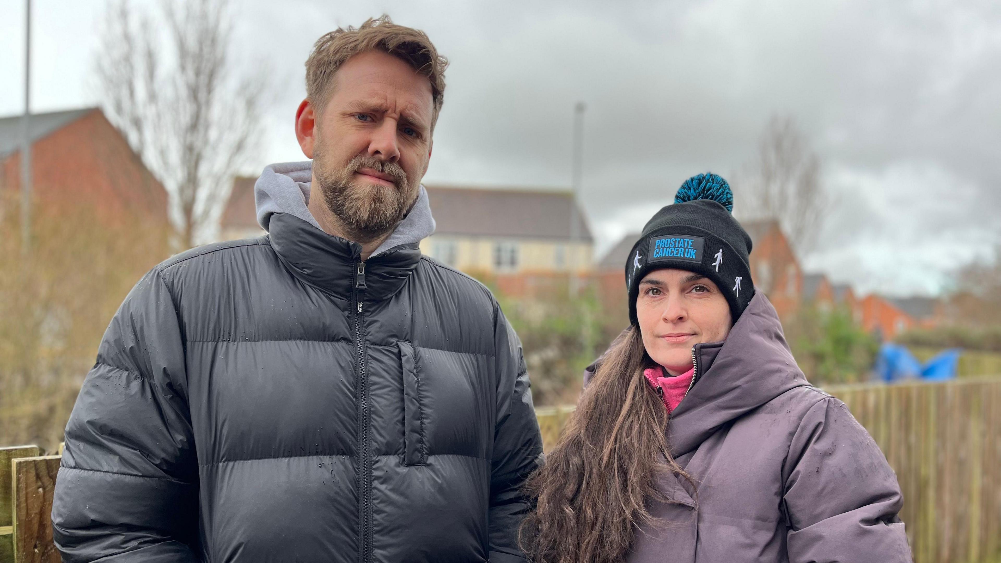 Chris and Nicola Day-Coiley stood together with winter coats on. Chris is wearing a black coat, has blond-ish hair and a beard. Nicola is shorter than him and wearing a black beanie with a long brown ponytail over one shoulder. She is wearing a grey/purple coat.