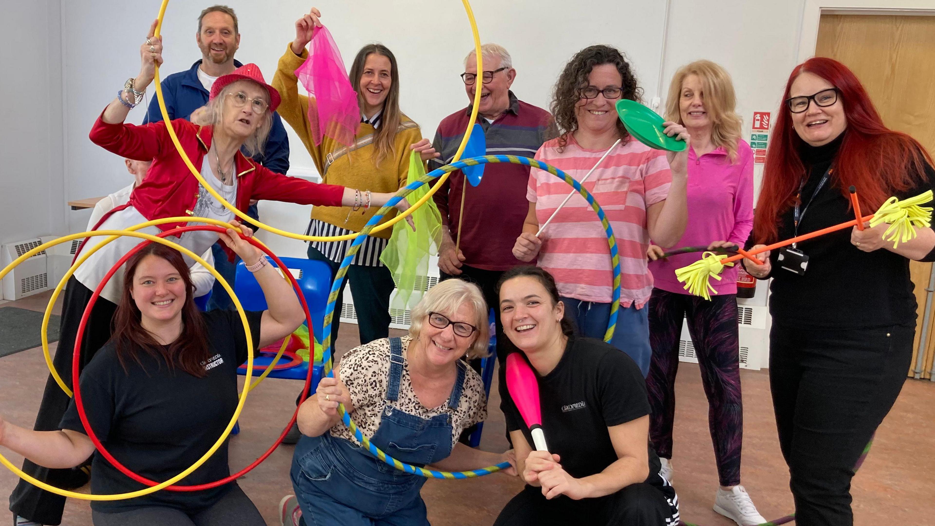 Members of the circus class are standing together in a group. They are holding up hoops and other various circus items. They are all laughing.