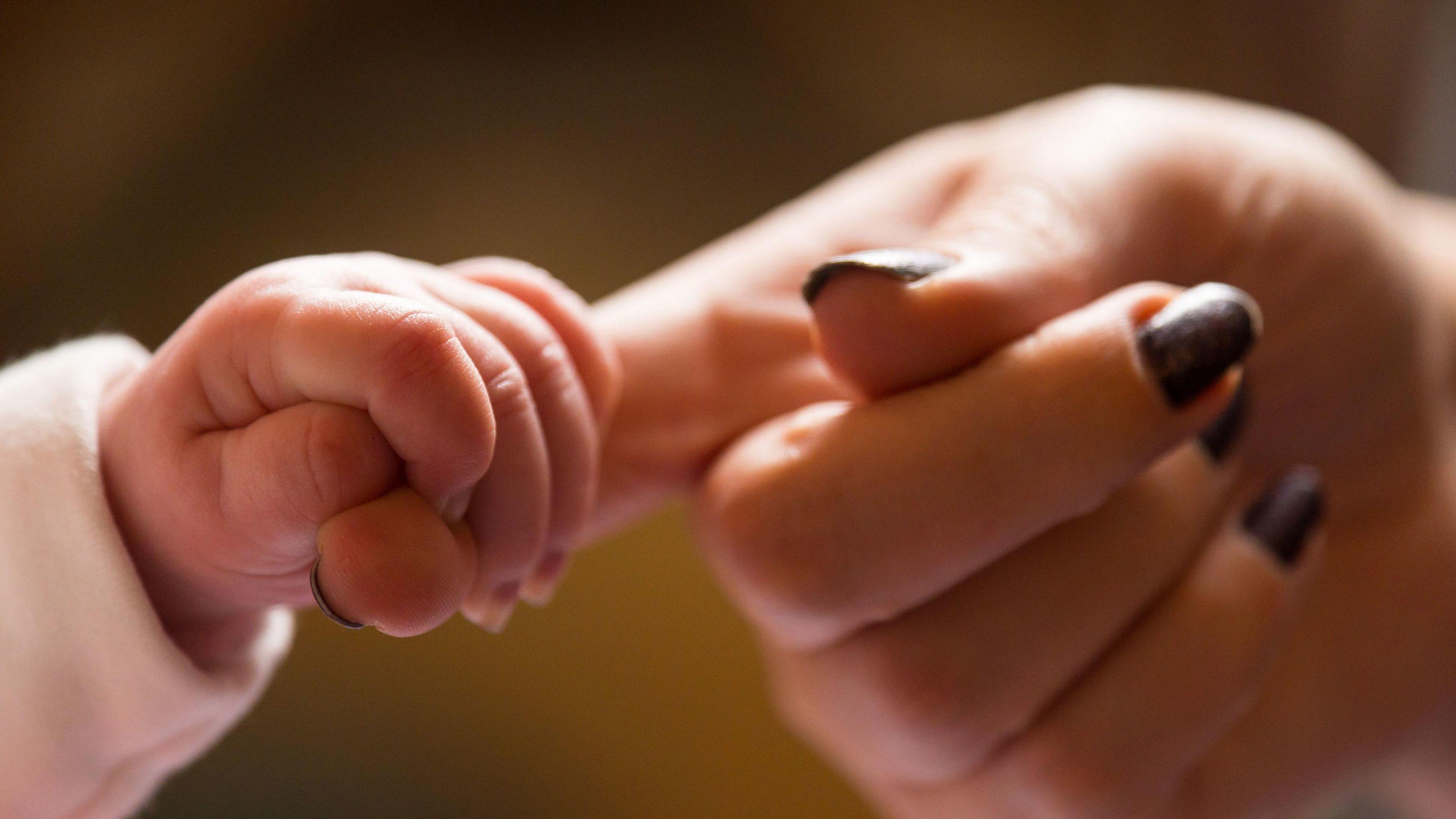 A baby holding their mother's finger