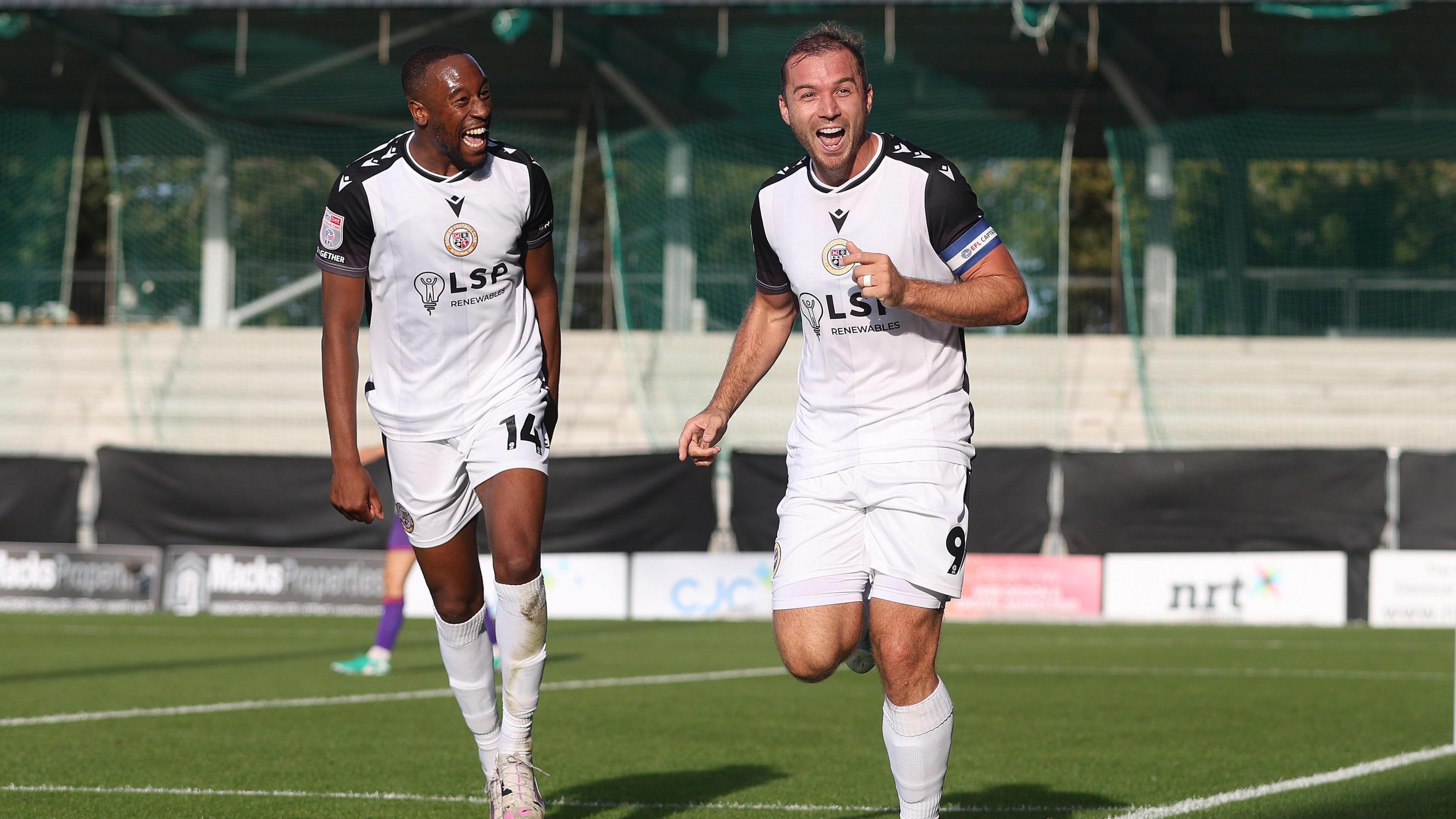 Nicke Kabamba and Michael Cheek celebrate while wearing their white Bromley kits in their game against Gillingham in September