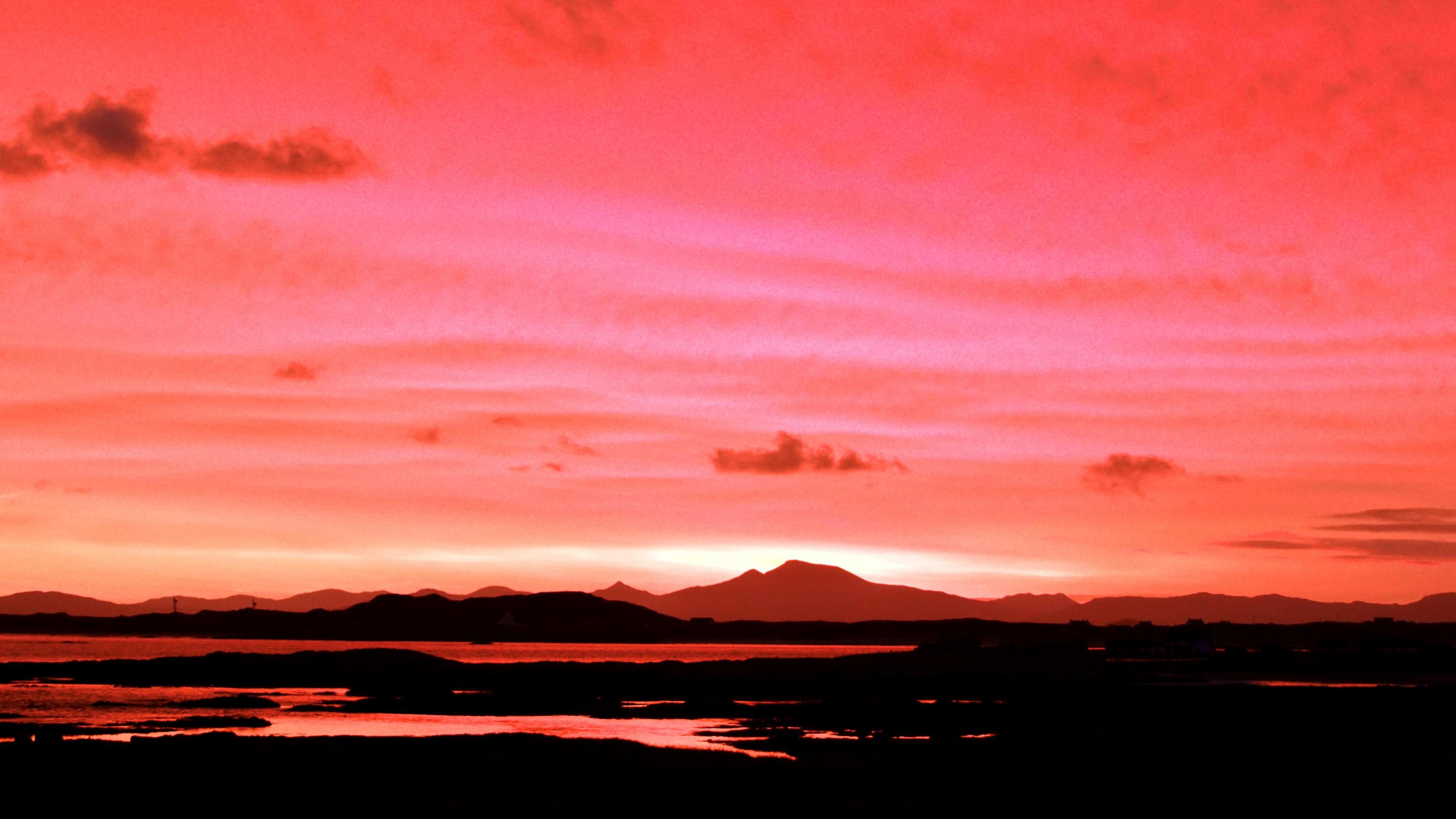 Vivid pink, red and orange landscape image at sunset with hills visible in the far distance