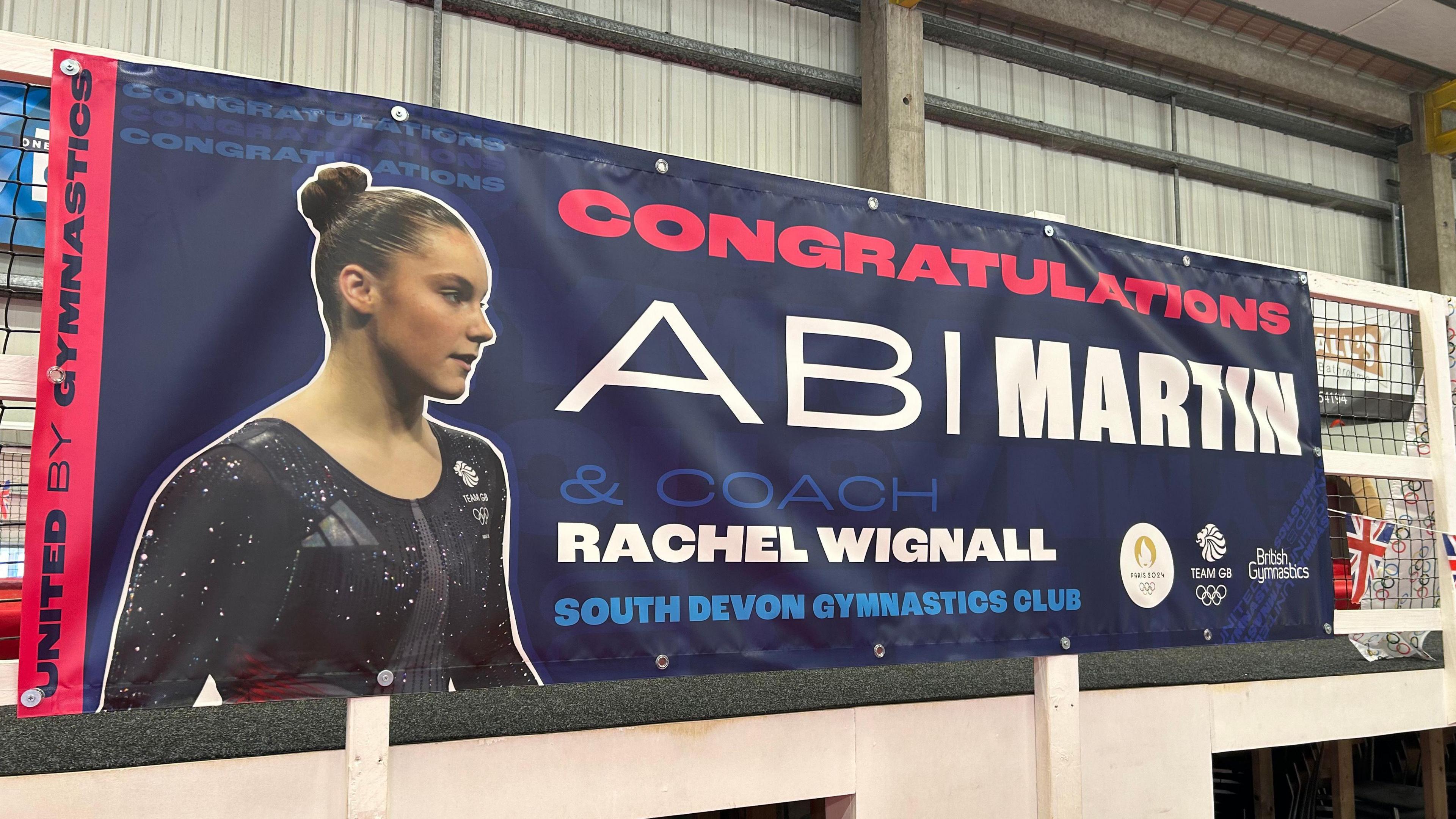 A banner with a photo of Abi Martin wearing her Team GB leotard saying congratulations to her and her coach Rachel Wignall for reaching the Olympic Games in Paris