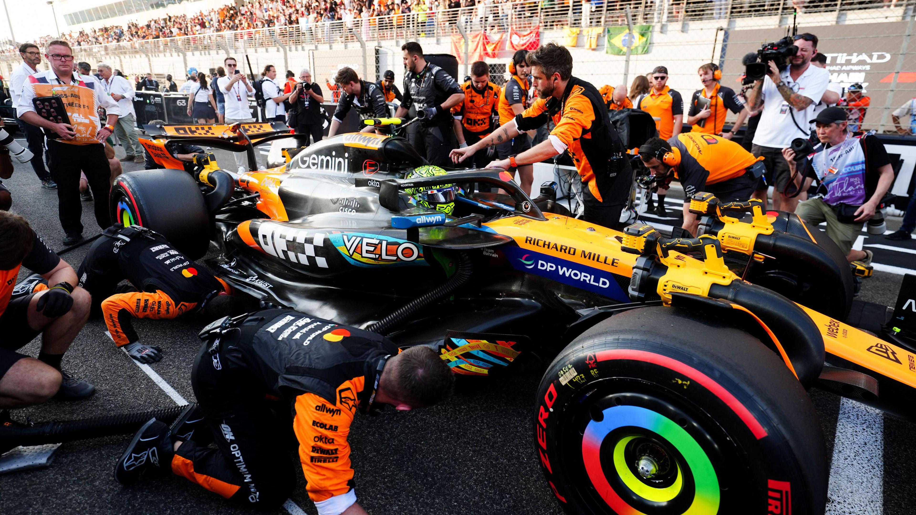 F1 driver Lando Norris gets into his car whilst teams attend to the vehicle