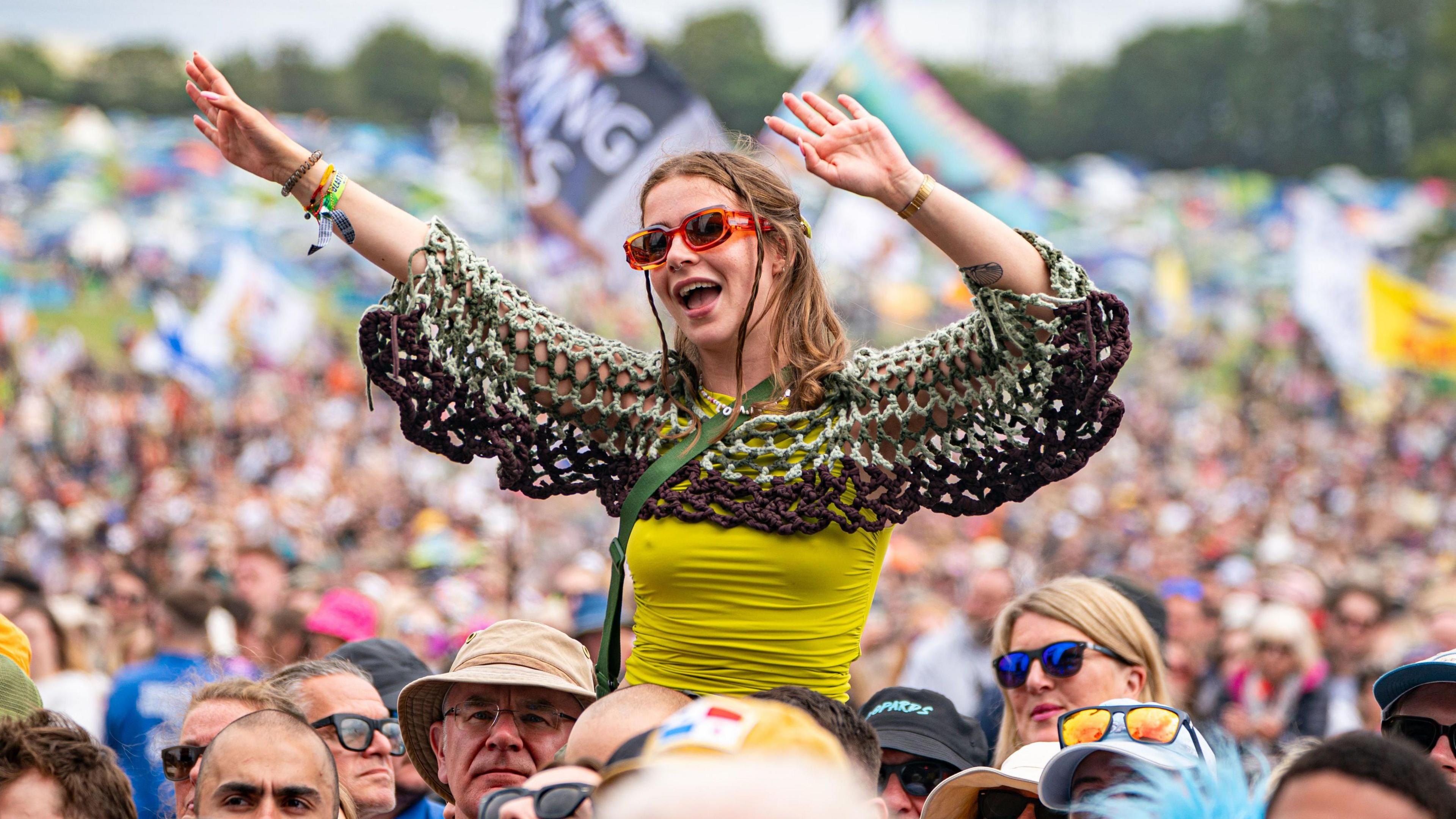 A woman sitting on someone's shoulders in the crowd whilst waving her hands