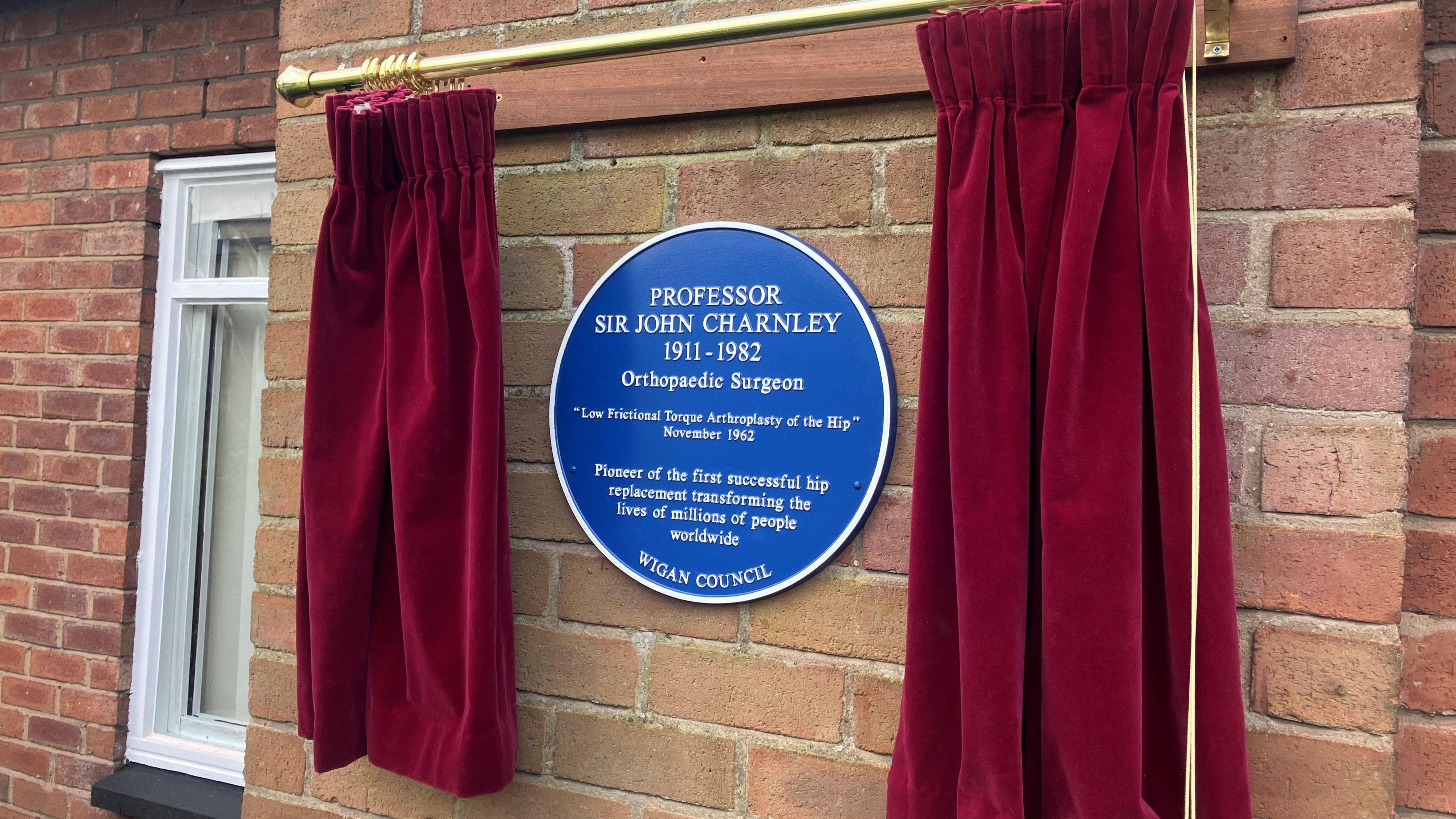 Photograph of a blue plaque on a brick wall at Wrightington Hospital