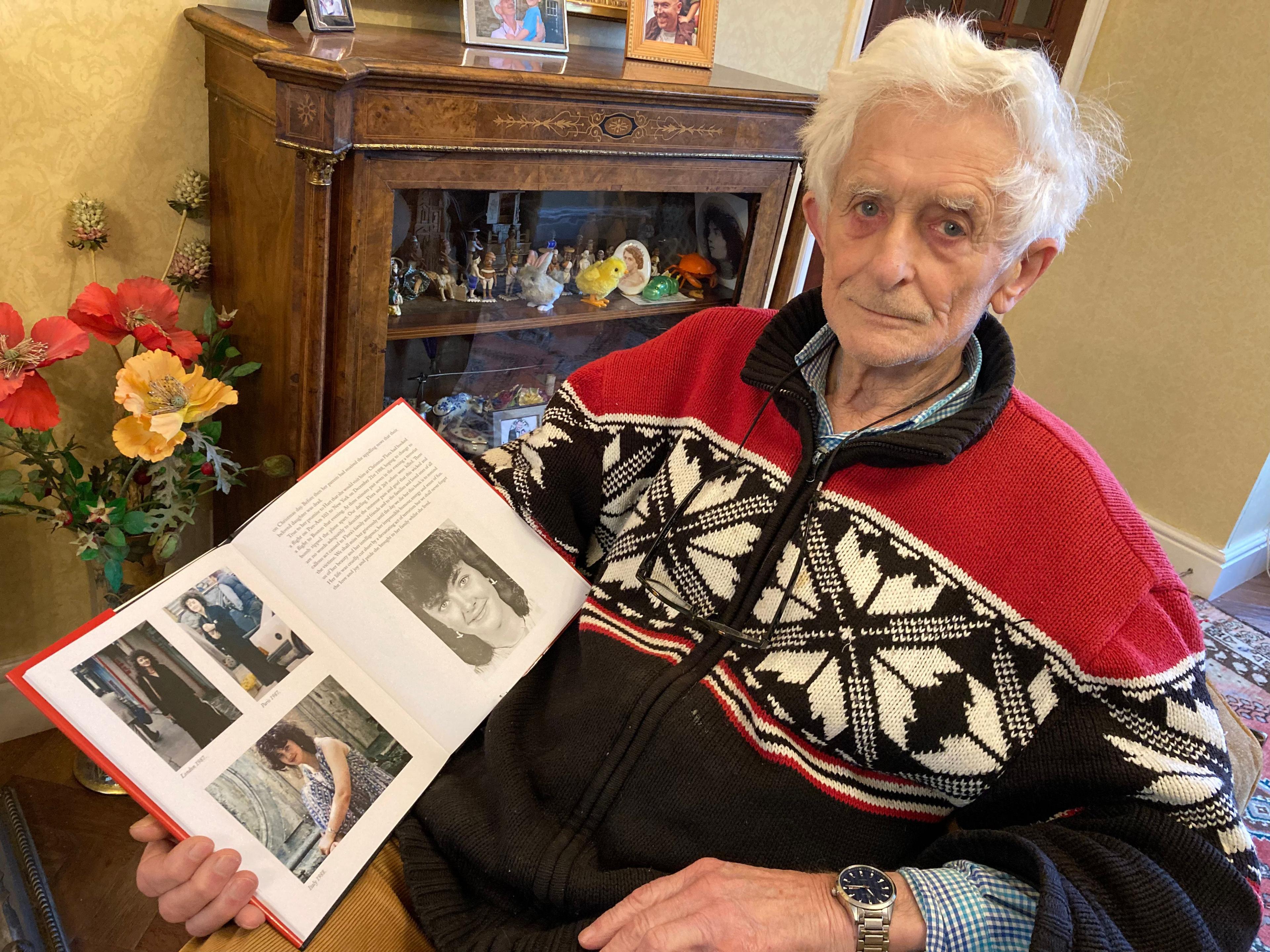 Dr Jim Swire sits at home holding a photo album which pictures his late daughter. He is wearing a red, white and blue jumper and has white hair