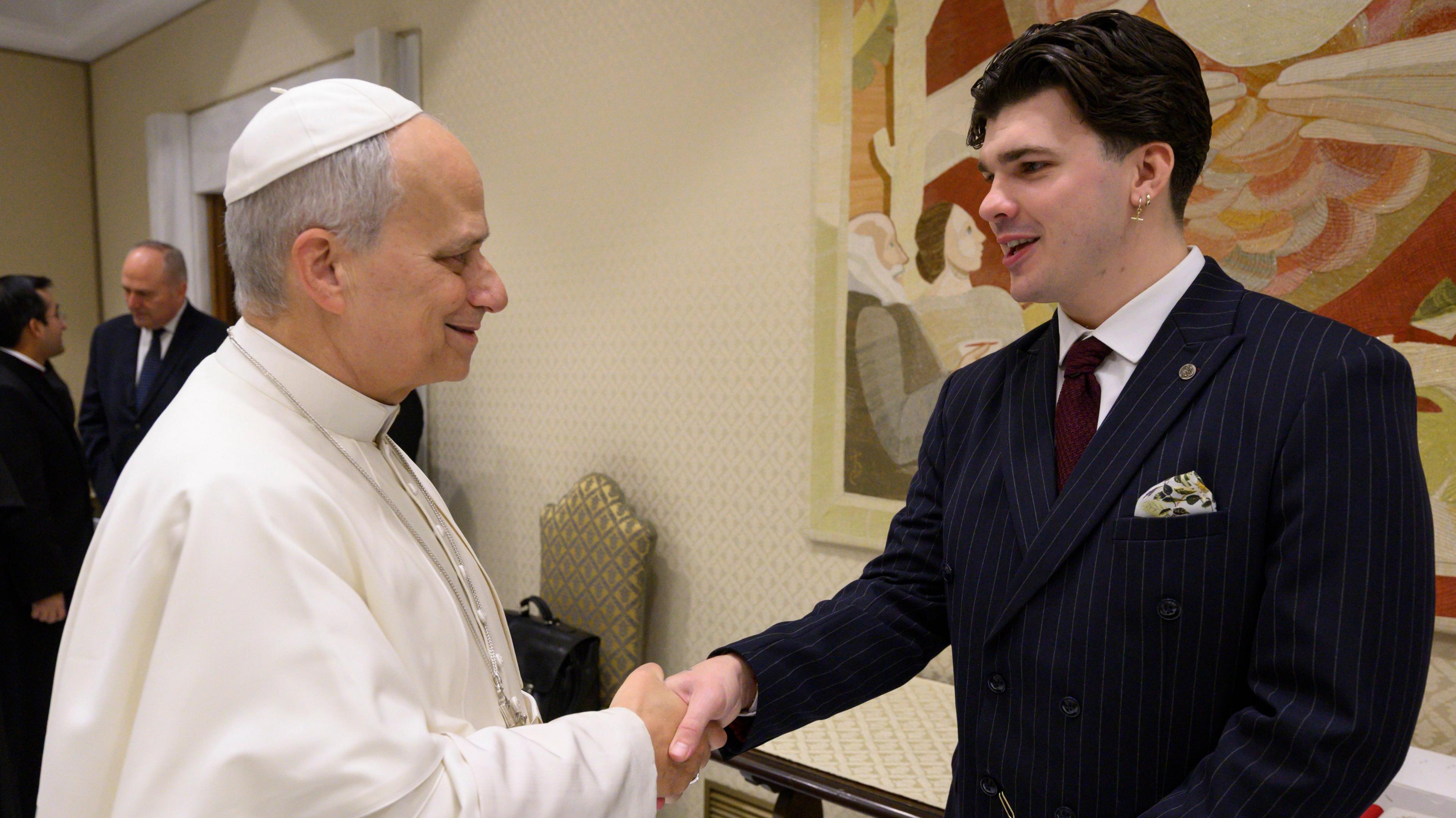 The Pope, wearing white shakes hands with Harry Clark, who is wearing a black suit. 