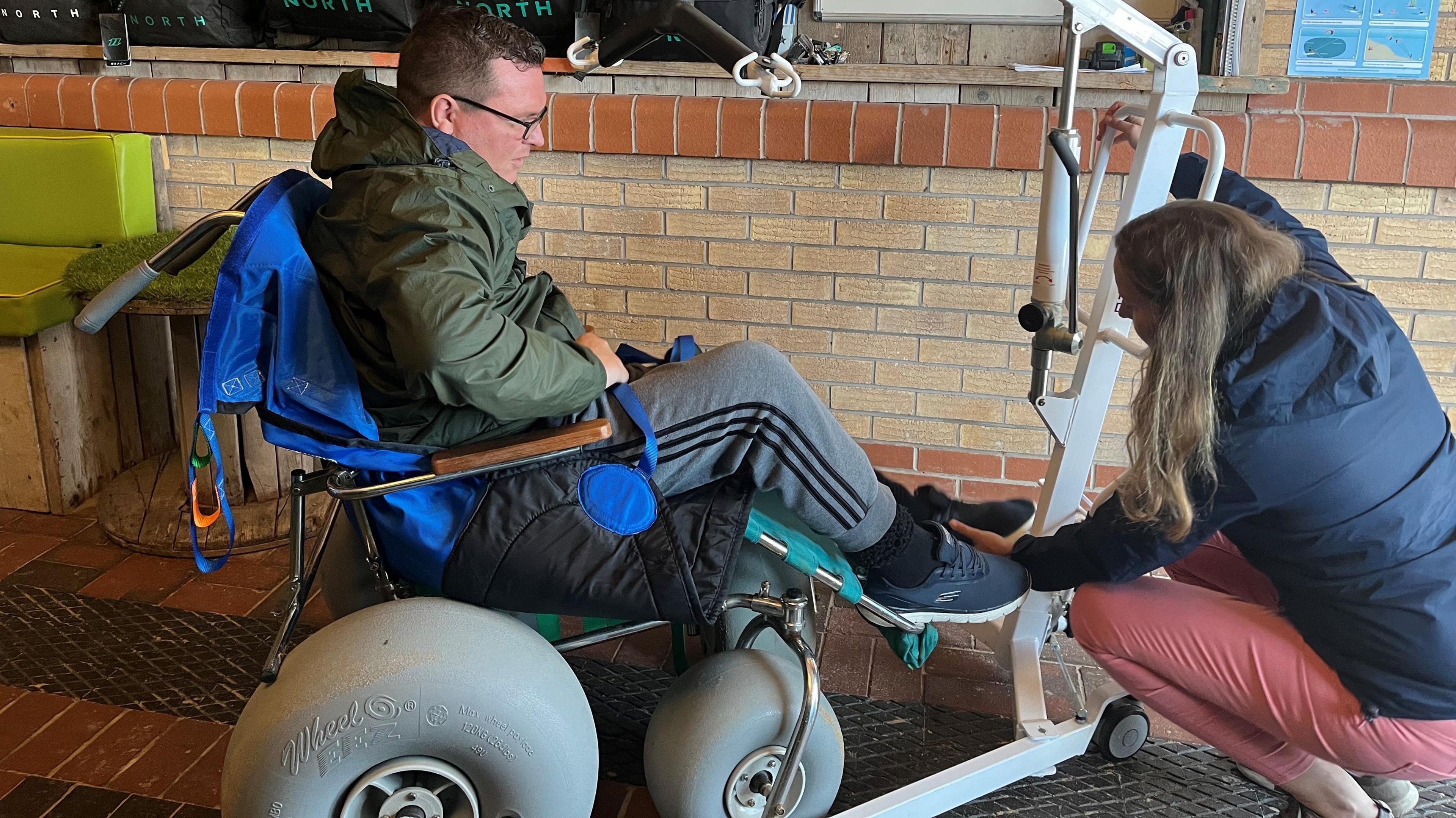 Shane Robins is helped into a special beach wheelchair with the aid of a hoist and his carer