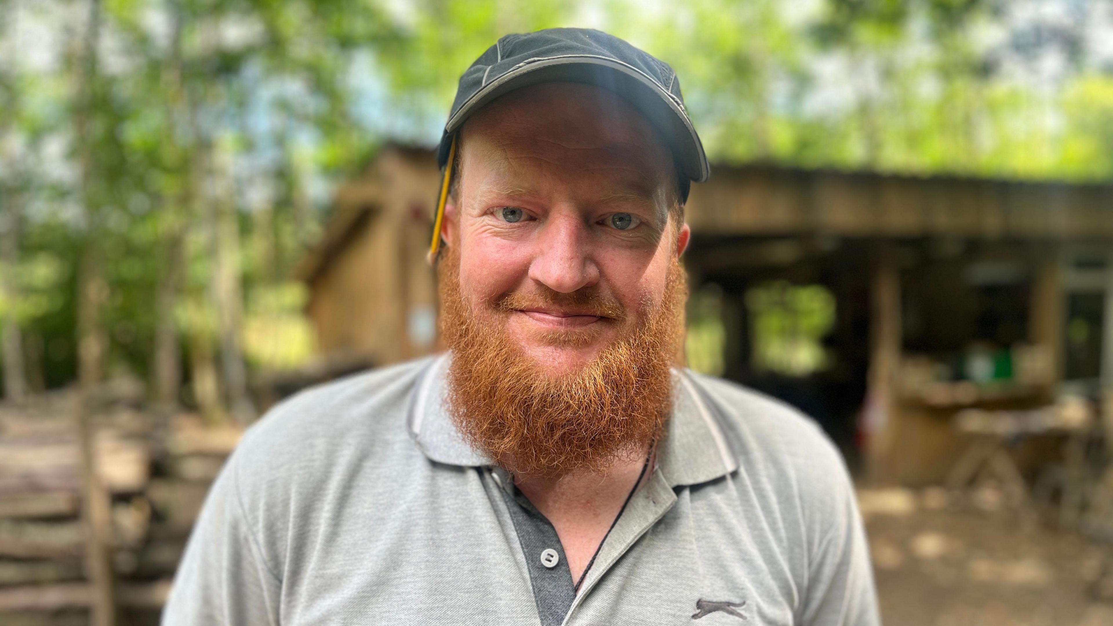 Dan wears a dark cap, he has a pencil tucked into his ear and a long ginger beard.