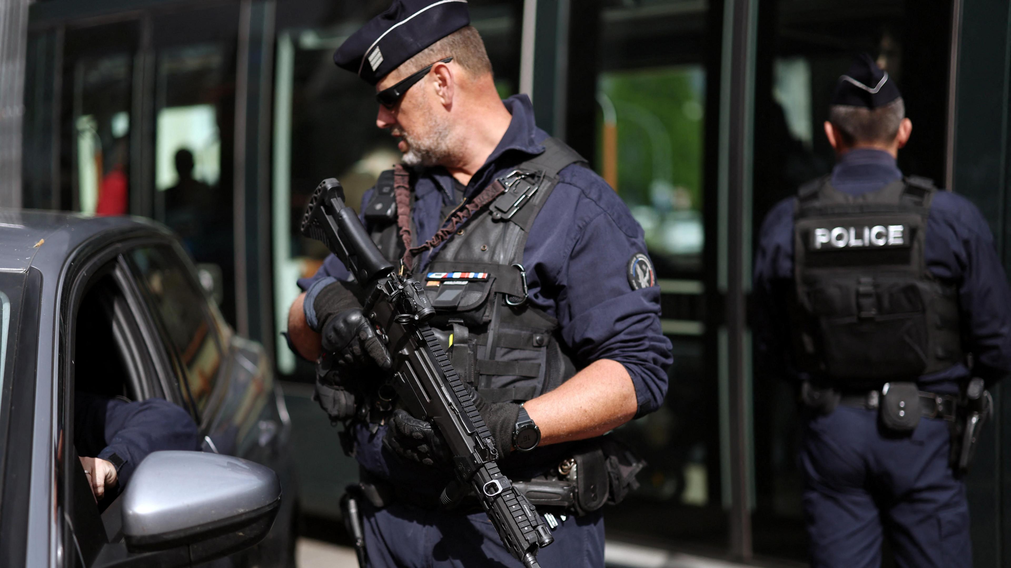 An armed police officer speaks to a driver through a car window
