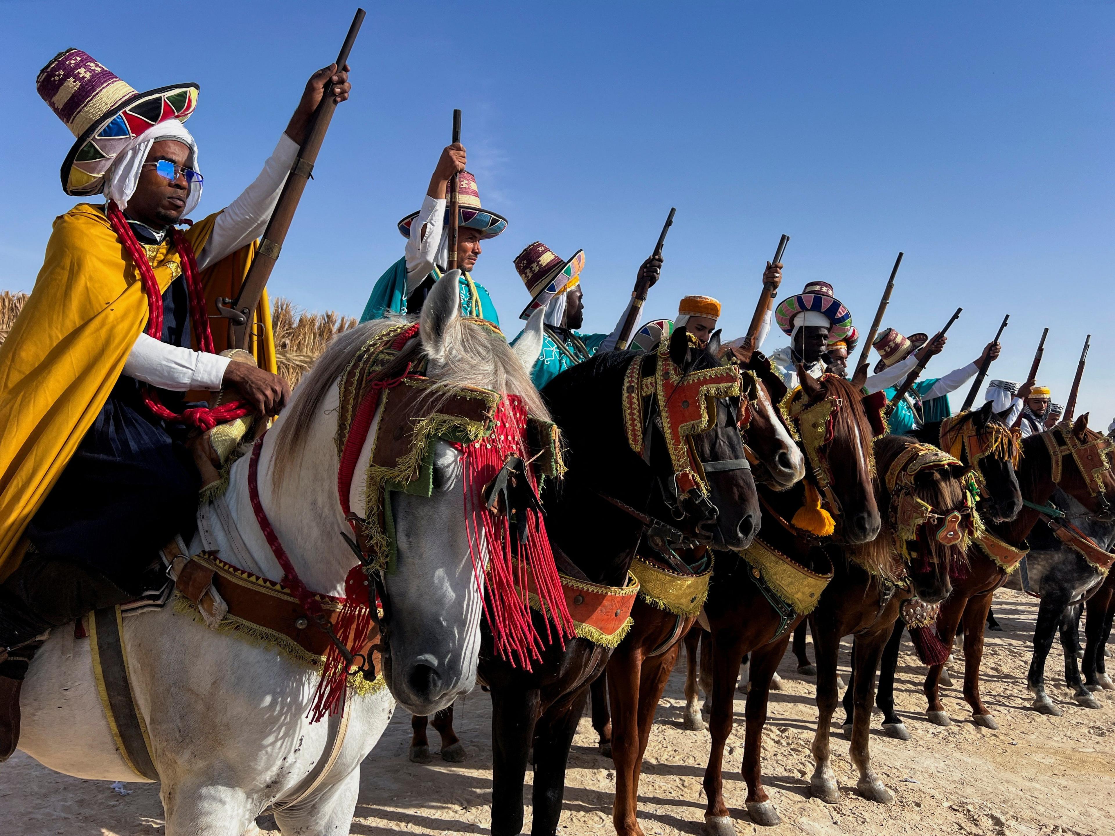 A line of men on horse point their rifles to the sky as they await to start their performance at the International Festival of Saharan Tourism in Oued Souf, Algeria - Saturday 16 November 2024