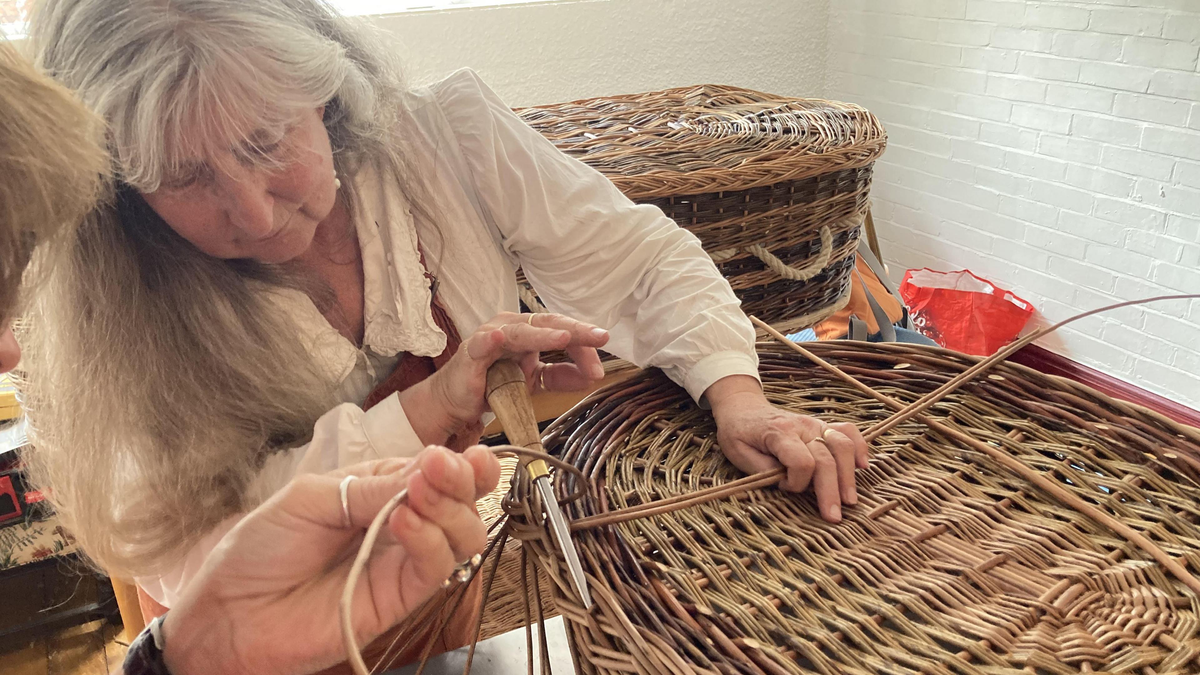 Helen holding a tool while weaving a coffin out of willow