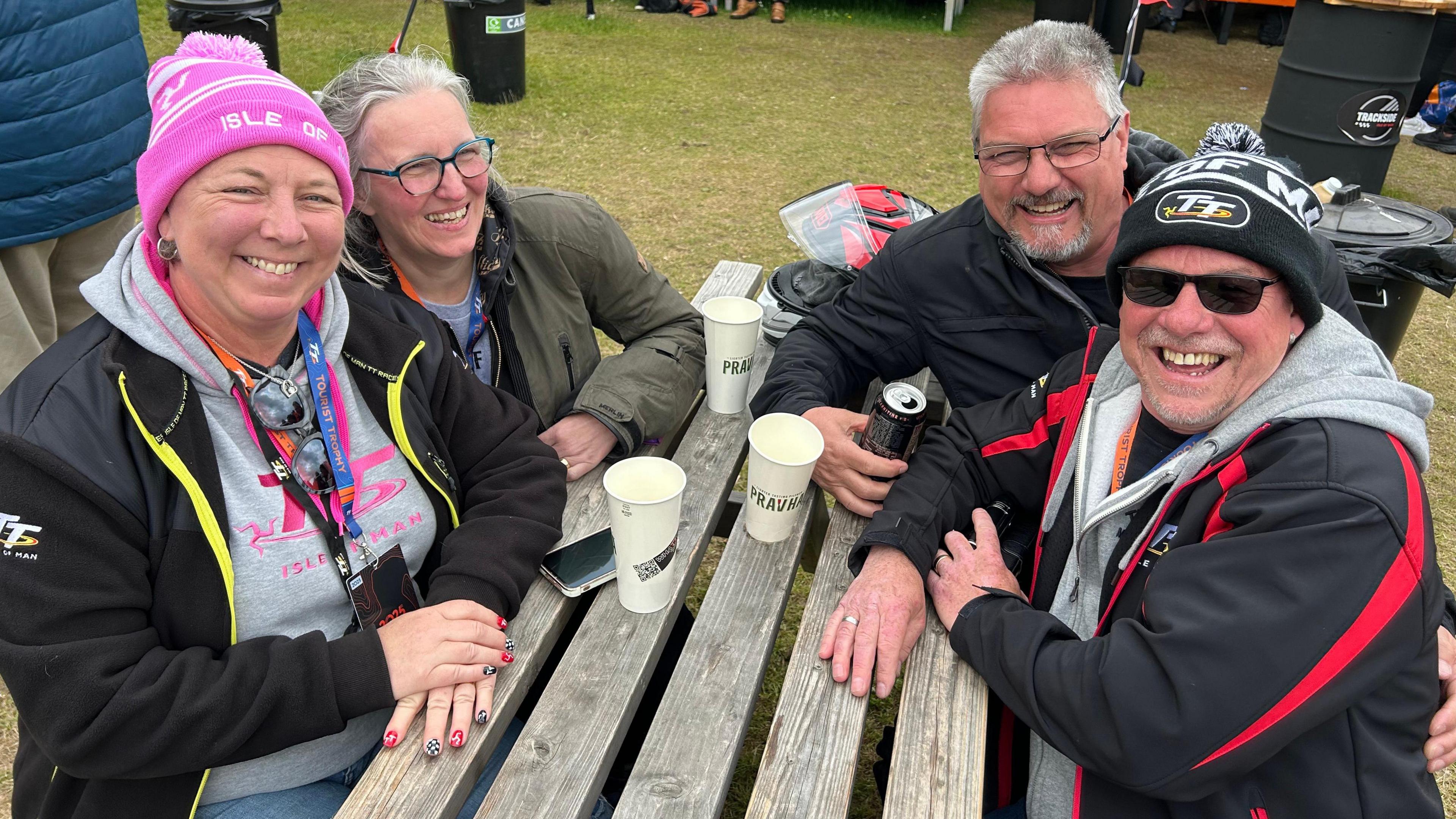 Two couples in big coats and hat sit around a table and smile.