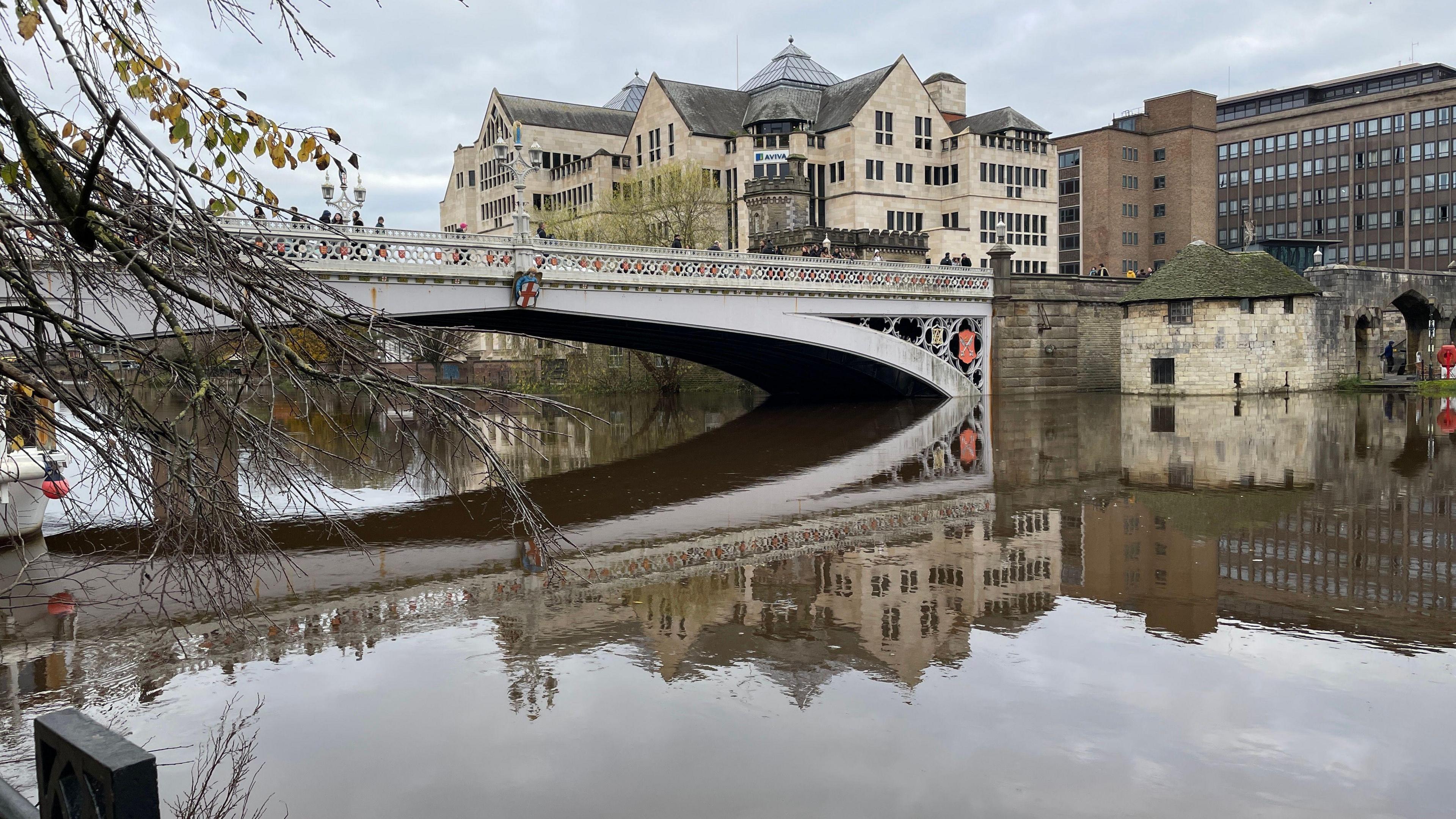 The River Ouse in York. Lendal Bridge can be seen over the water. A tree is also in frame as well as several buildings.