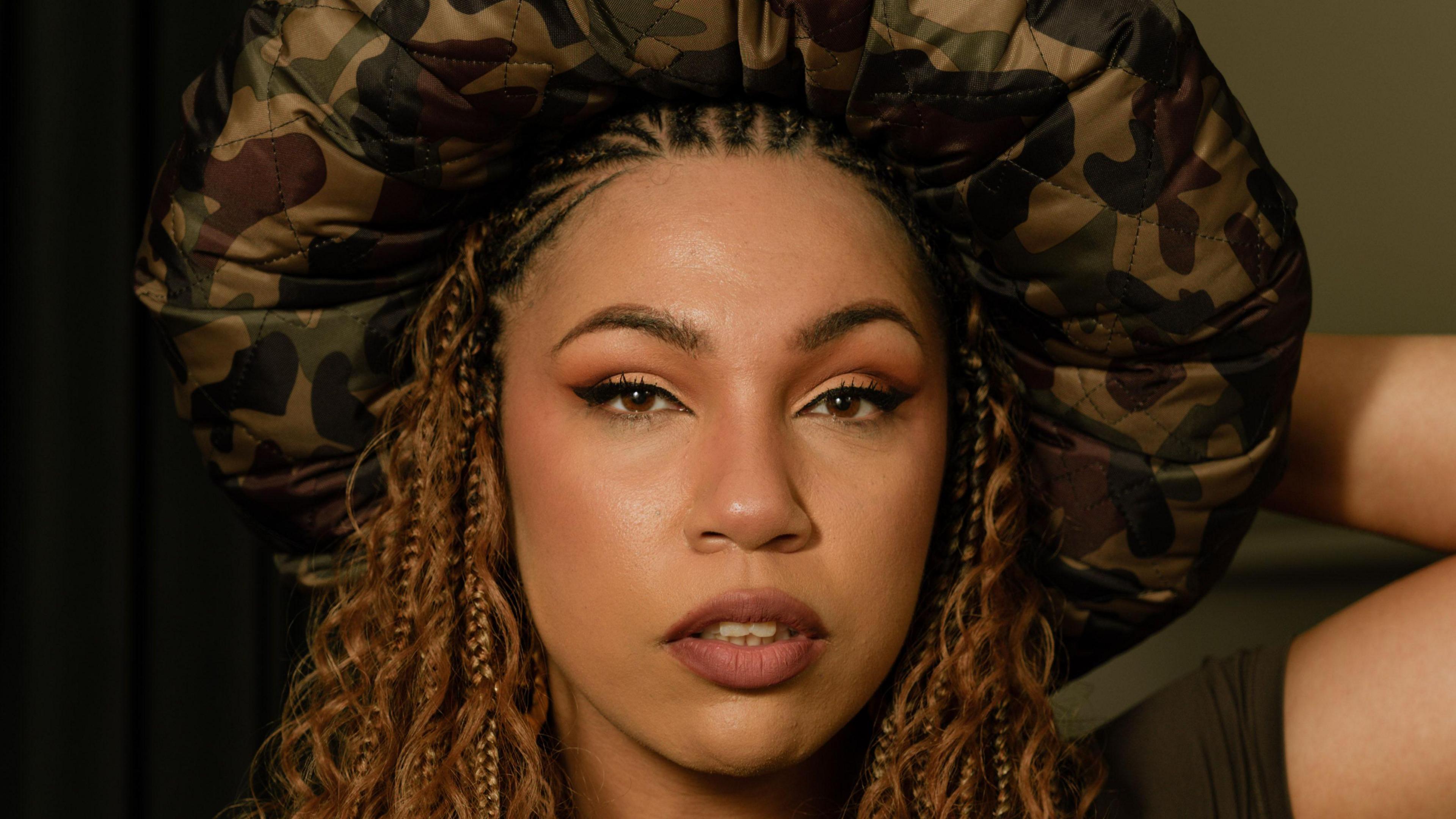 Eva Lazurus looking into the camera with brown eyes, light brown braids and a puffy, camouflage hat on