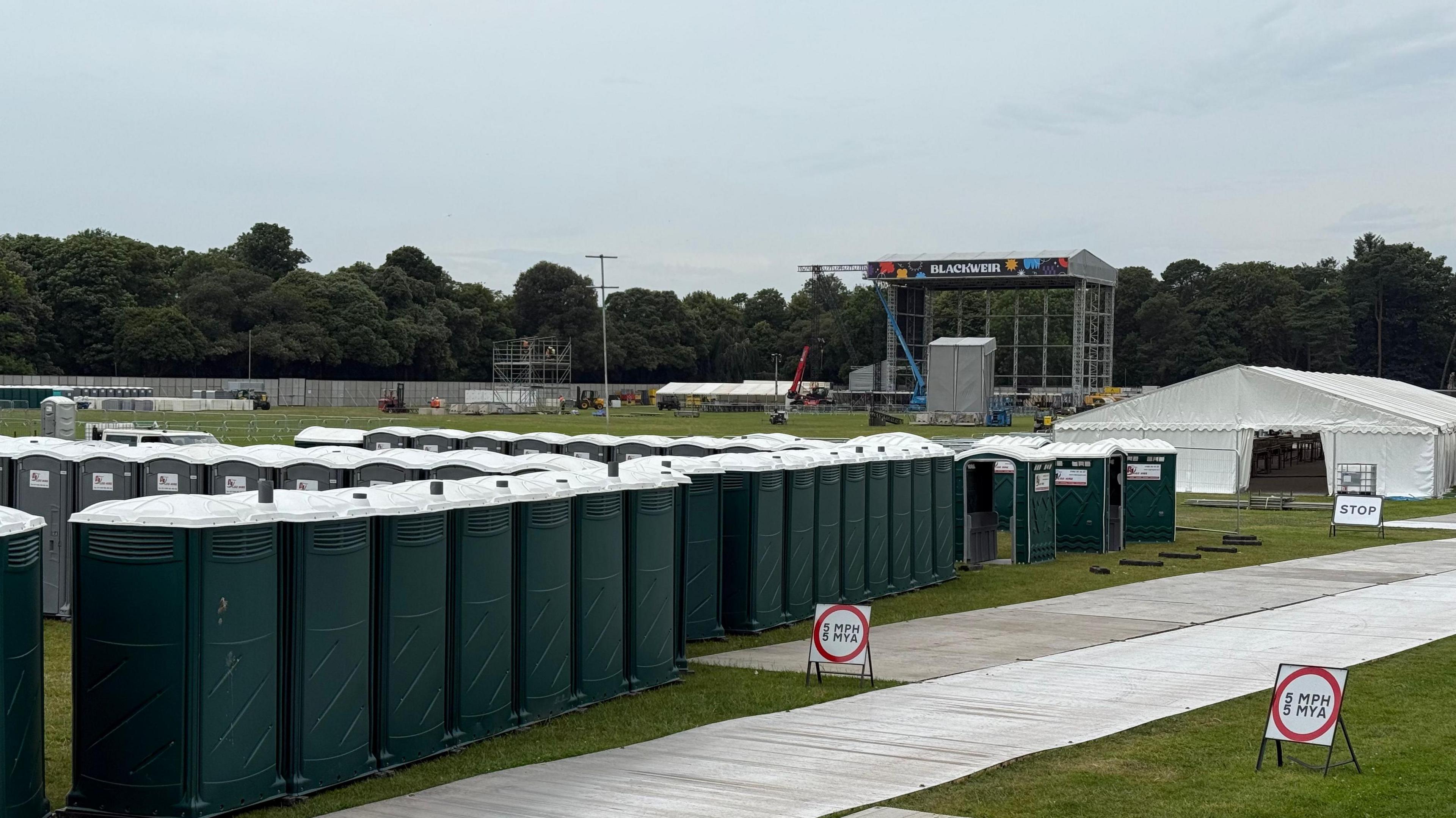 Rhes o doiledi portaloo o flaen llwyfan ar gae Blackweir 
