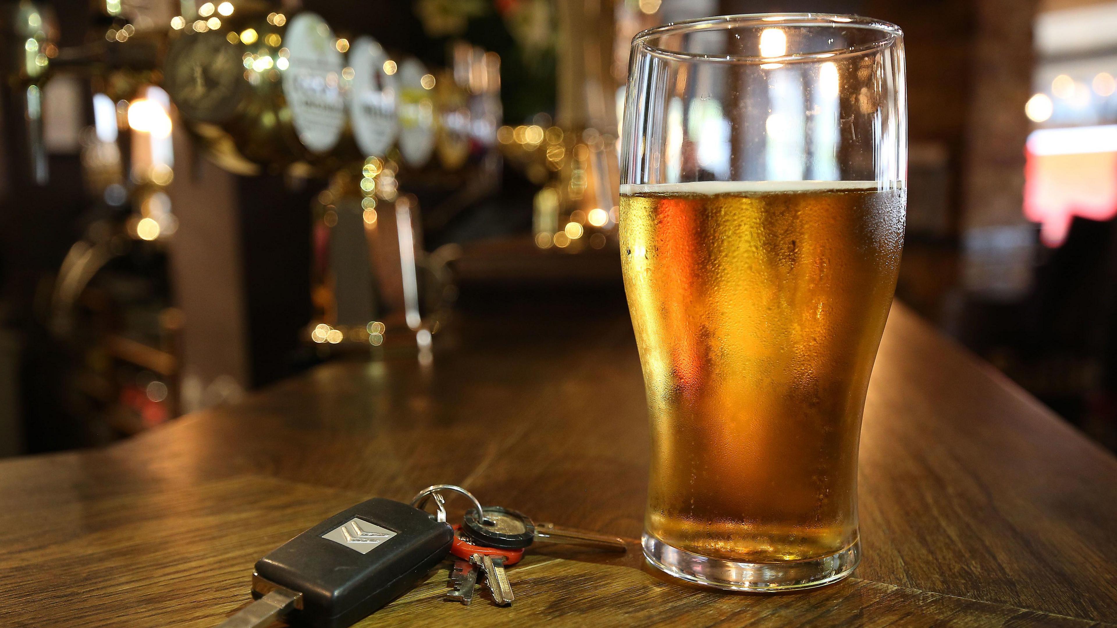 A pint of beer on the side of a bar next to a car key.