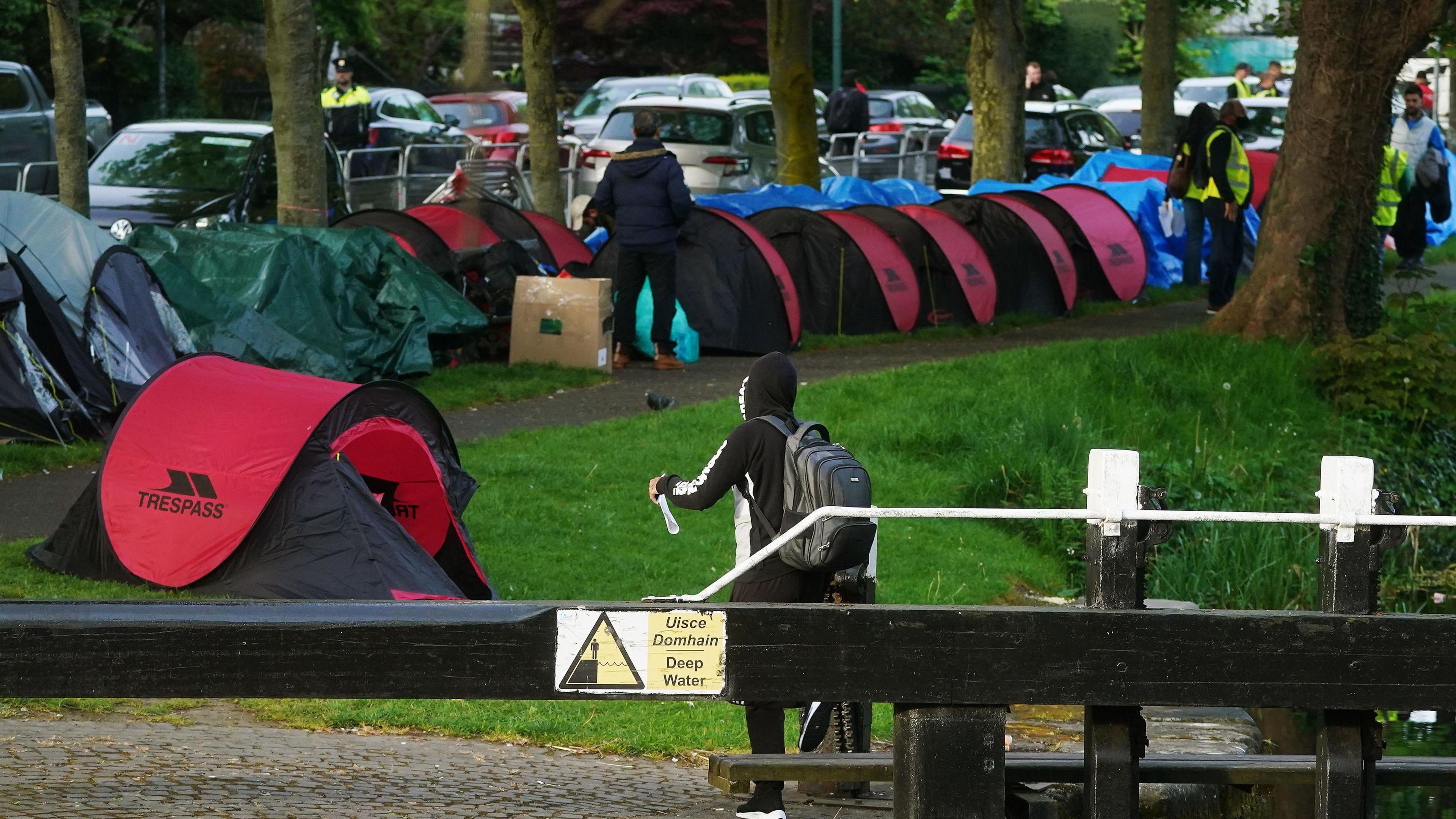 An early morning operation to remove tents which have been pitched by asylum seekers along a stretch of the Grand Canal, Dublin. There are numerous tents and people in high-viz jackets and a garda can be seen in the background.