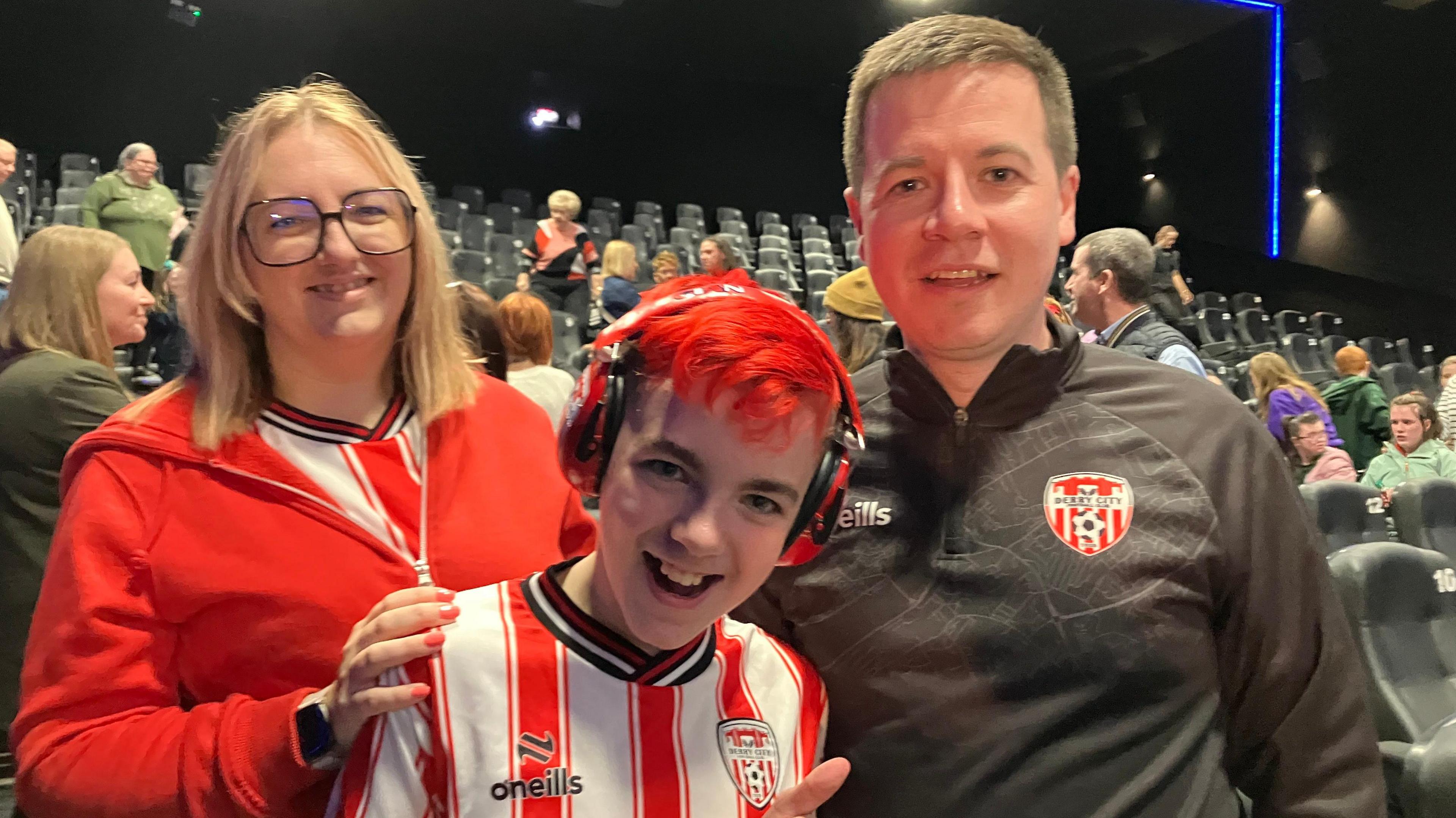 Cian has bright red hair and is seen smiling while wearing red ear protectors.
He is in a Derry City shirt and his parents are standing either side of him.
They are pictured in the movie theatre as a number of people are taking their seats.