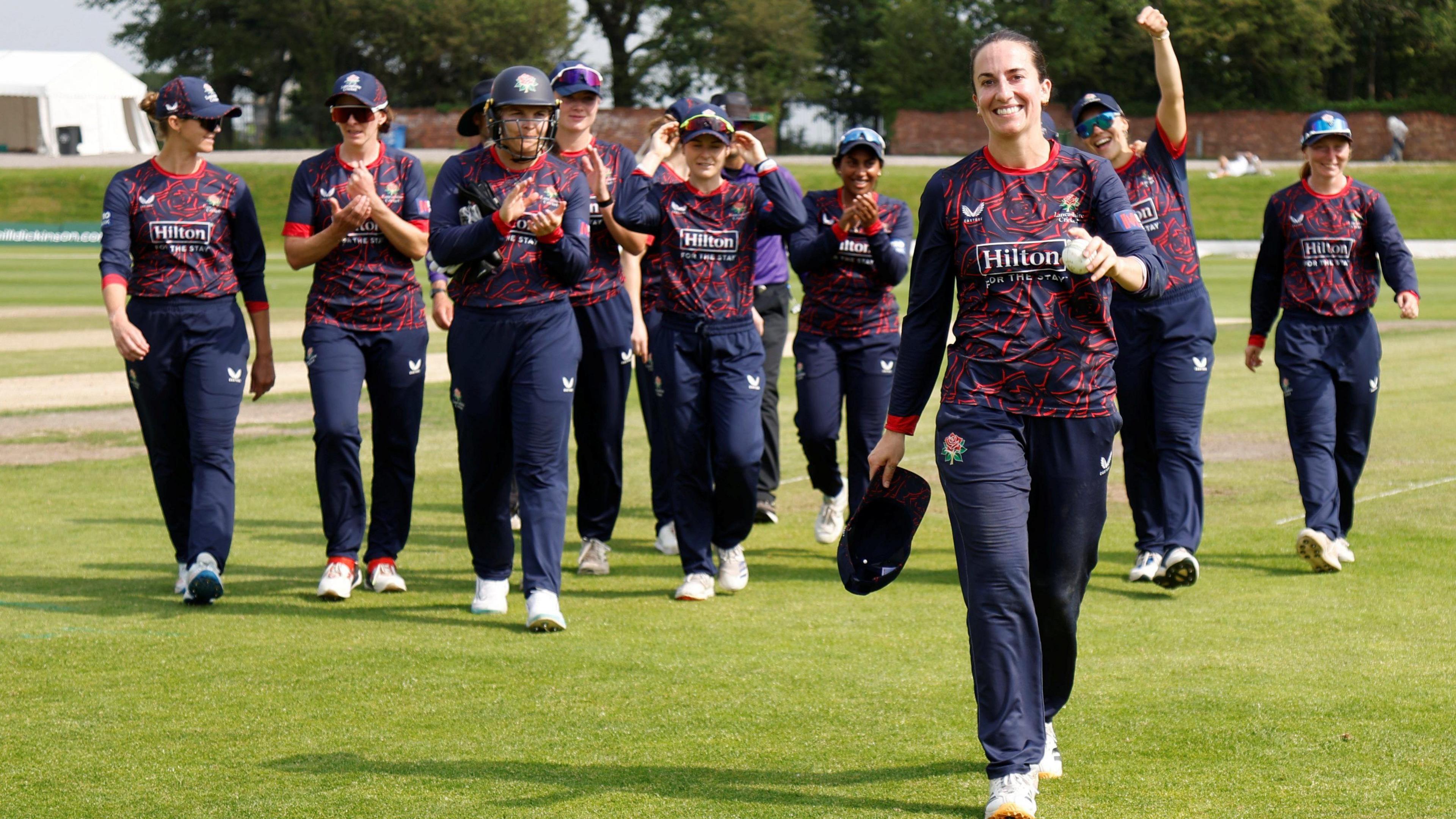 Fi Morris in the foreground leads Lancashire off the field with the rest of the team cheering behind her after taking 6-27 against Essex