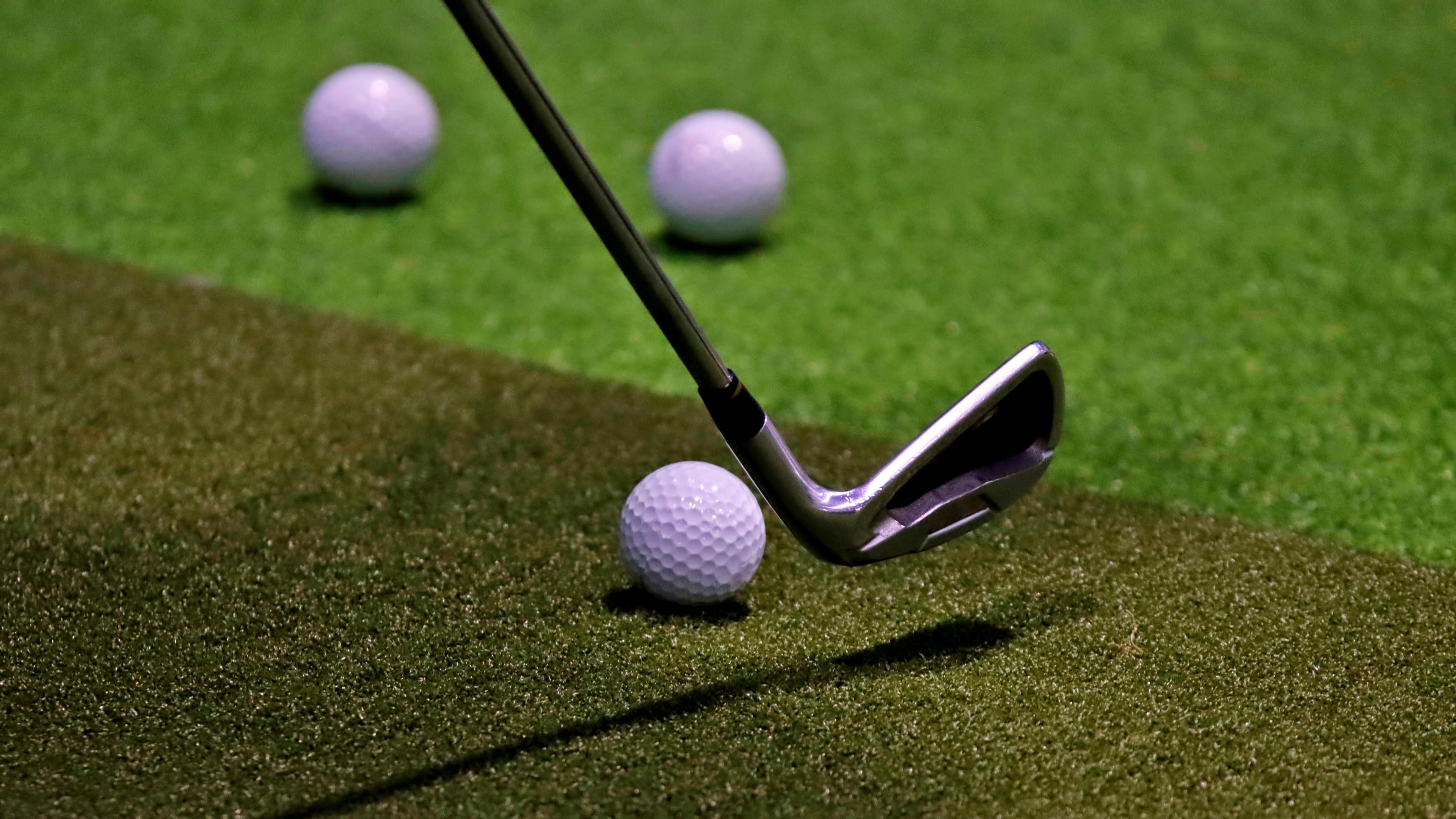 A golf club, poised to be swung towards a golf ball on a simulator