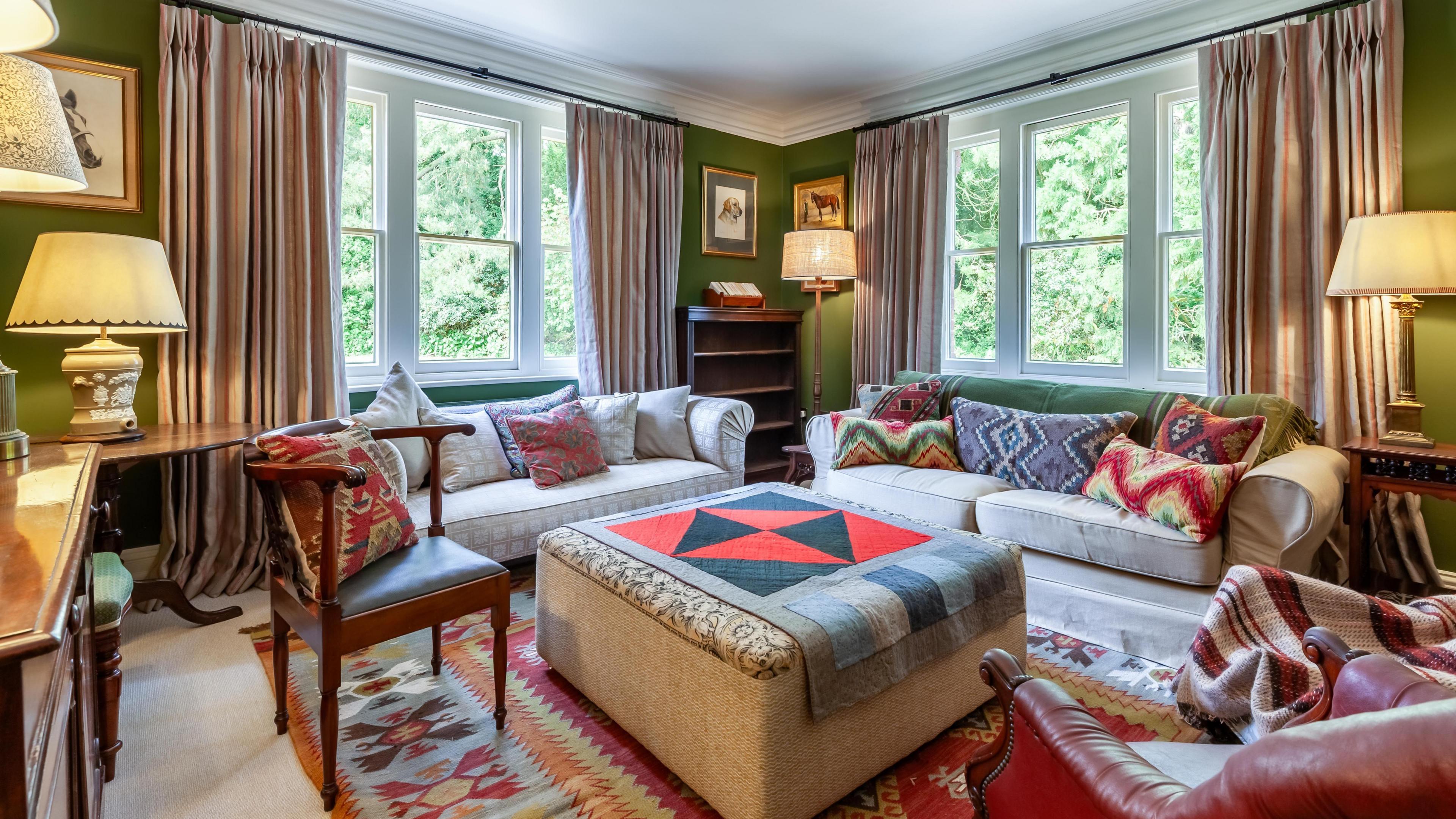 Internal view of the The Gardens House showing the living room which is carpeted with red rug and chair and two cream sofas.