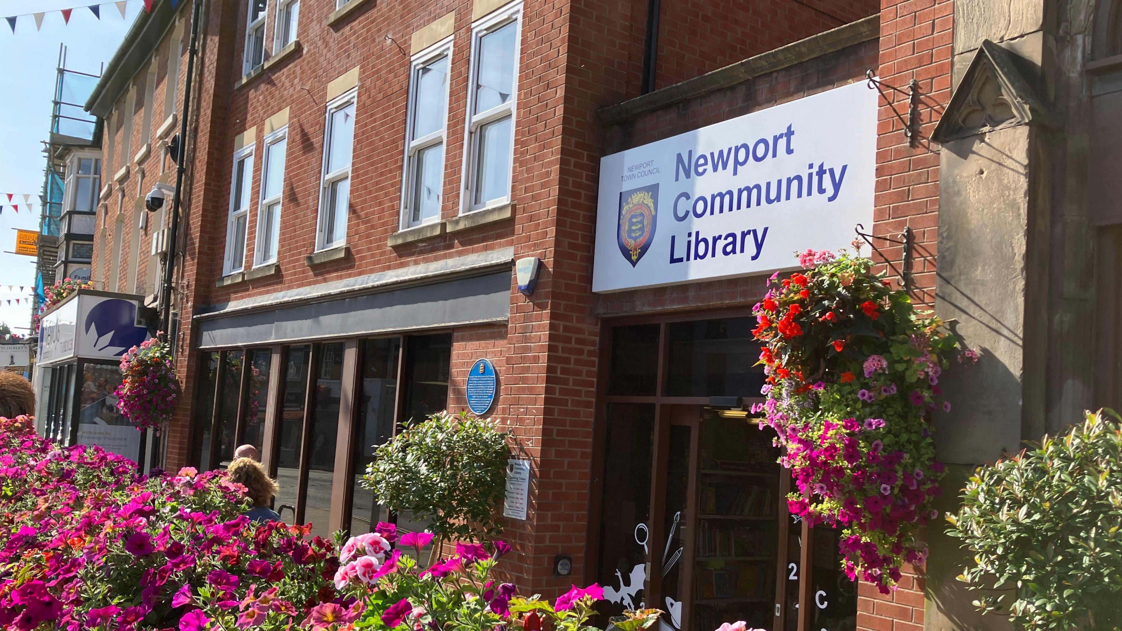 View of Newport library on a sunny day in August with hanging baskets in bloom on the exterior wall and pink flower beds in the foreground