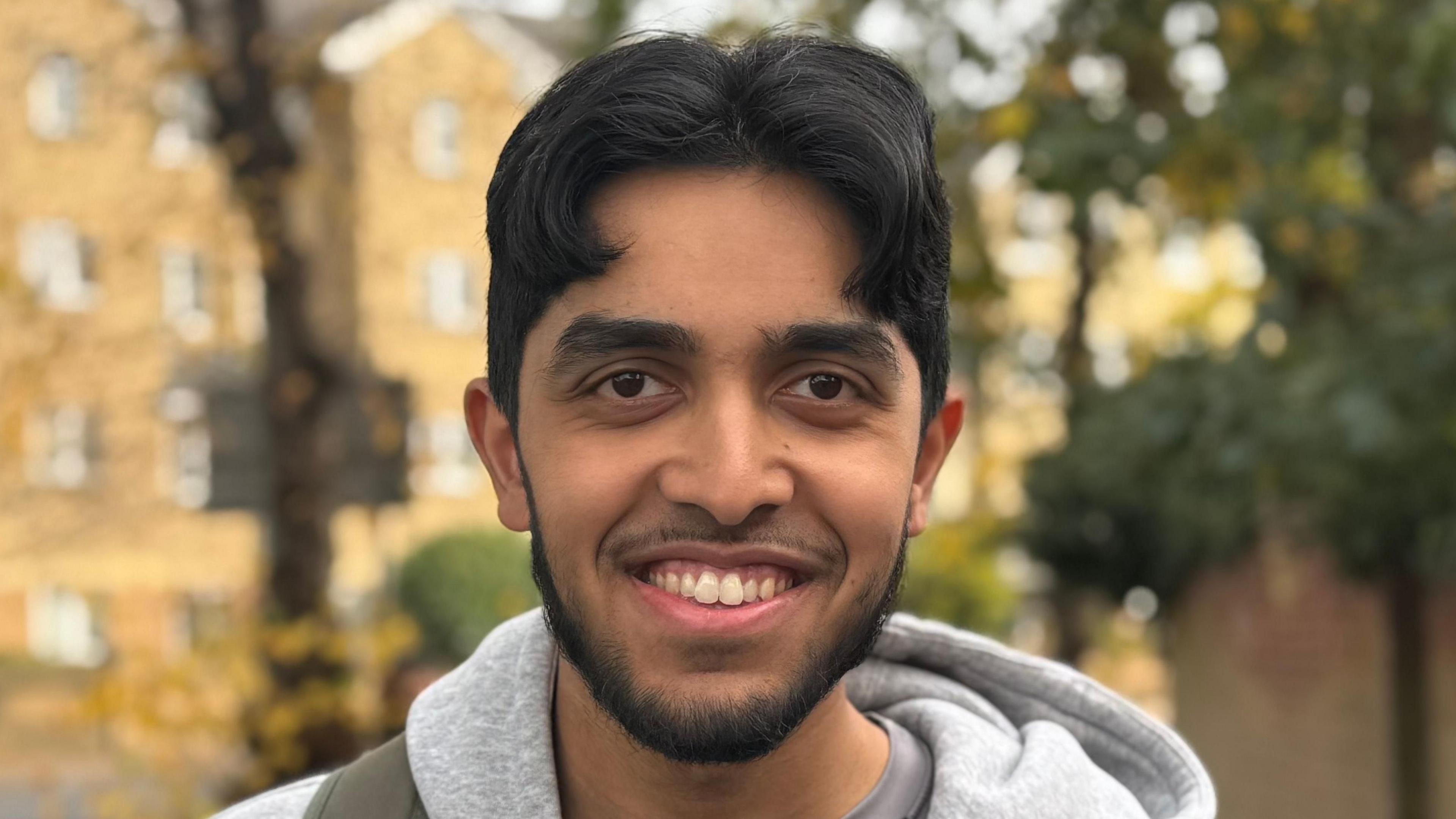 A close-up head and shoulders image of Yaseen Moksud. He is wearing a grey hoody and smiling while looking into the camera.