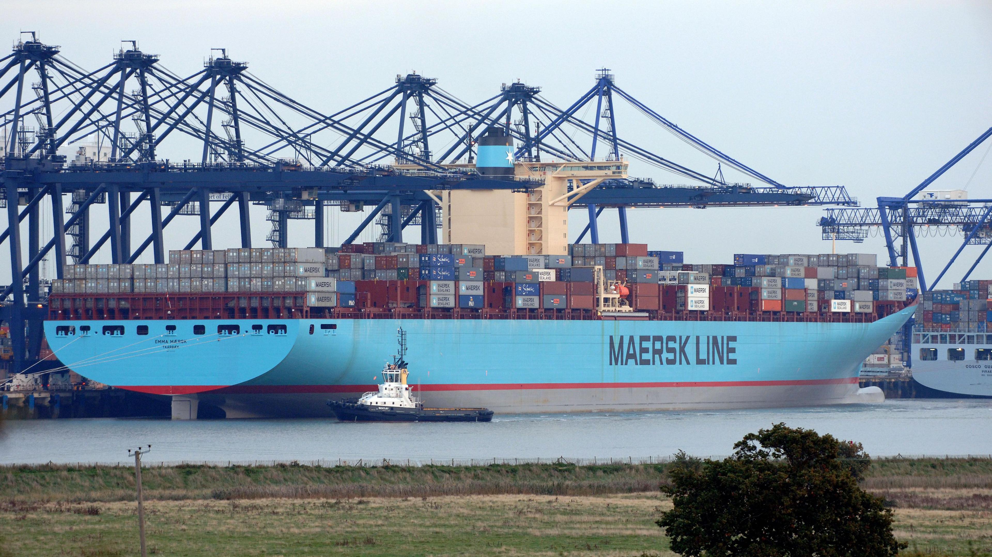 A Maersk Line ship with a blue hull loaded with containers and docked at the Port of Felixstowe. A row of blue cranes is on the quayside. In the foreground is the opposite bank of the estuary at Shotley Gate.