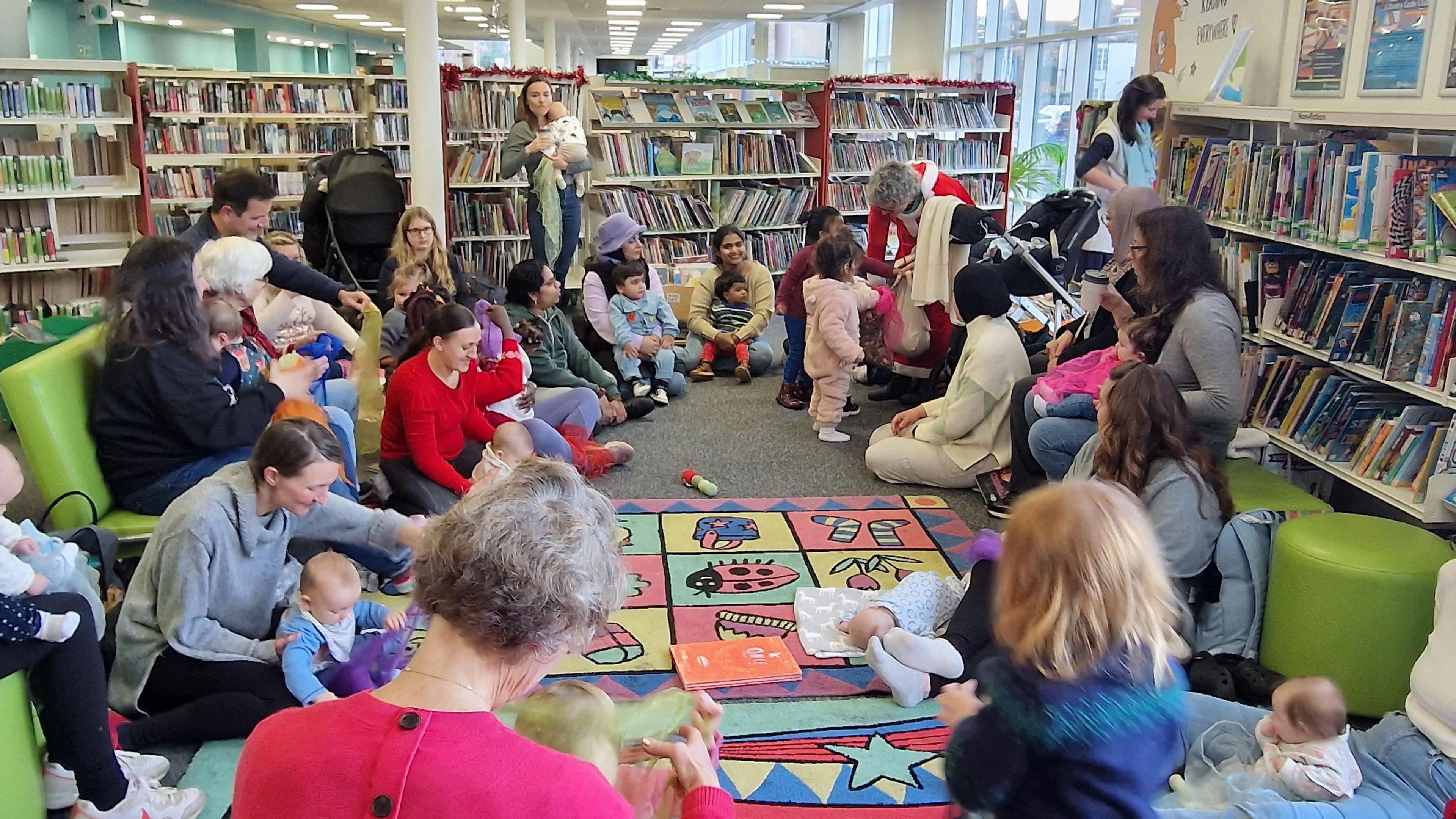 A group of parents sat down playing with their young children on the floor of a library