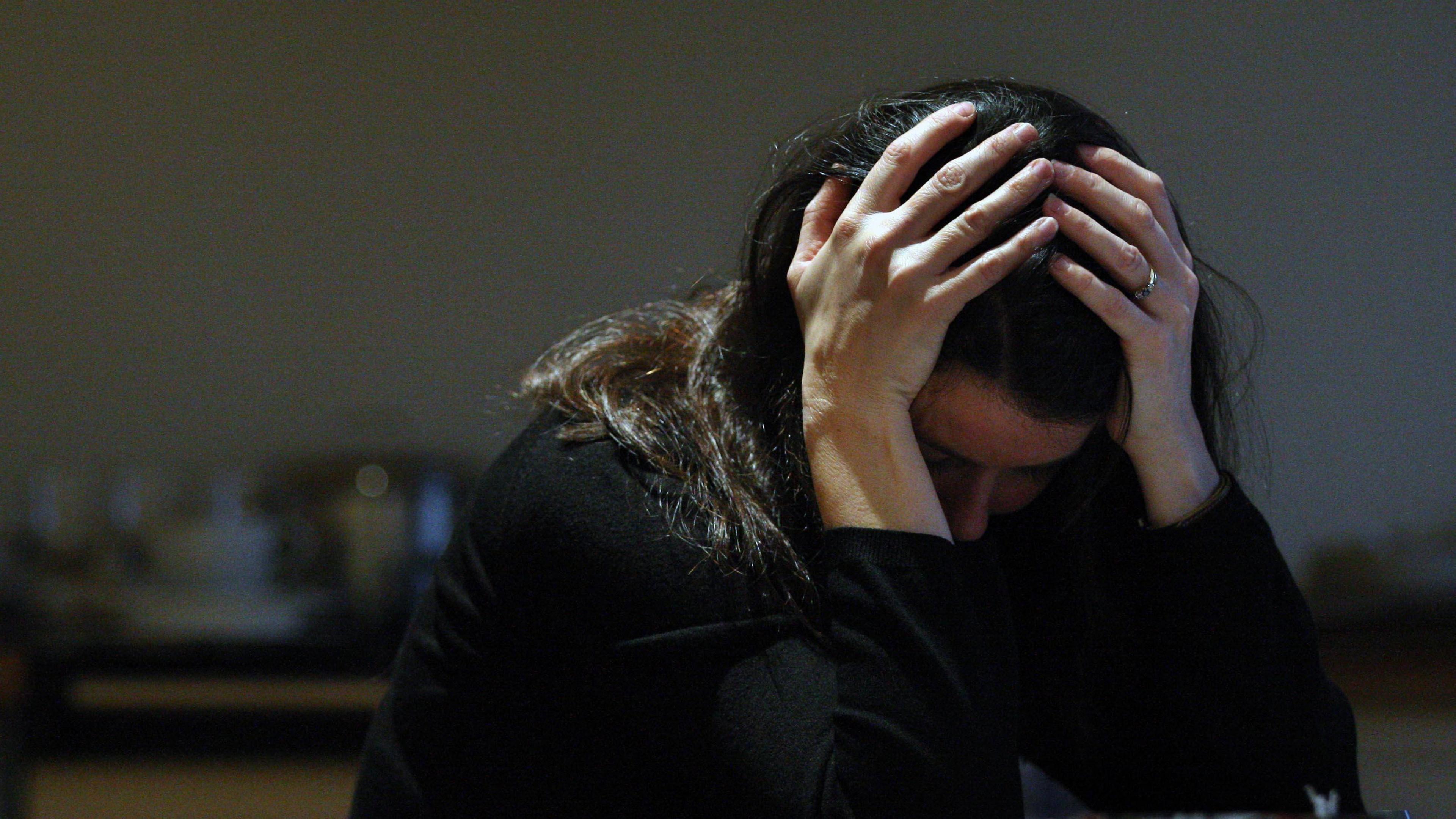 A woman with her head in her hands, sits in a dark room