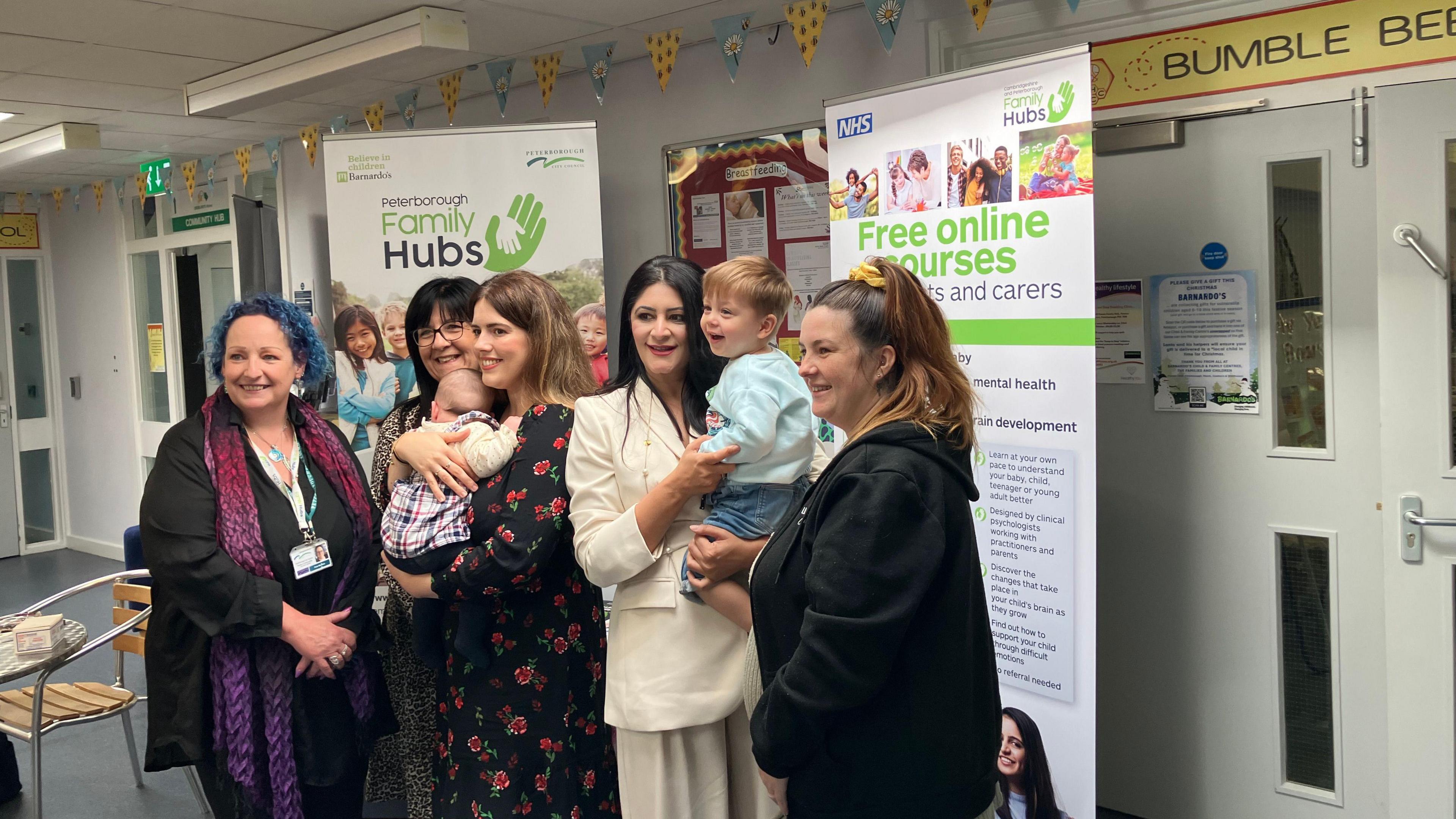 Group picture of council staff and users with their babies in their arms standing in front of the family hub poster