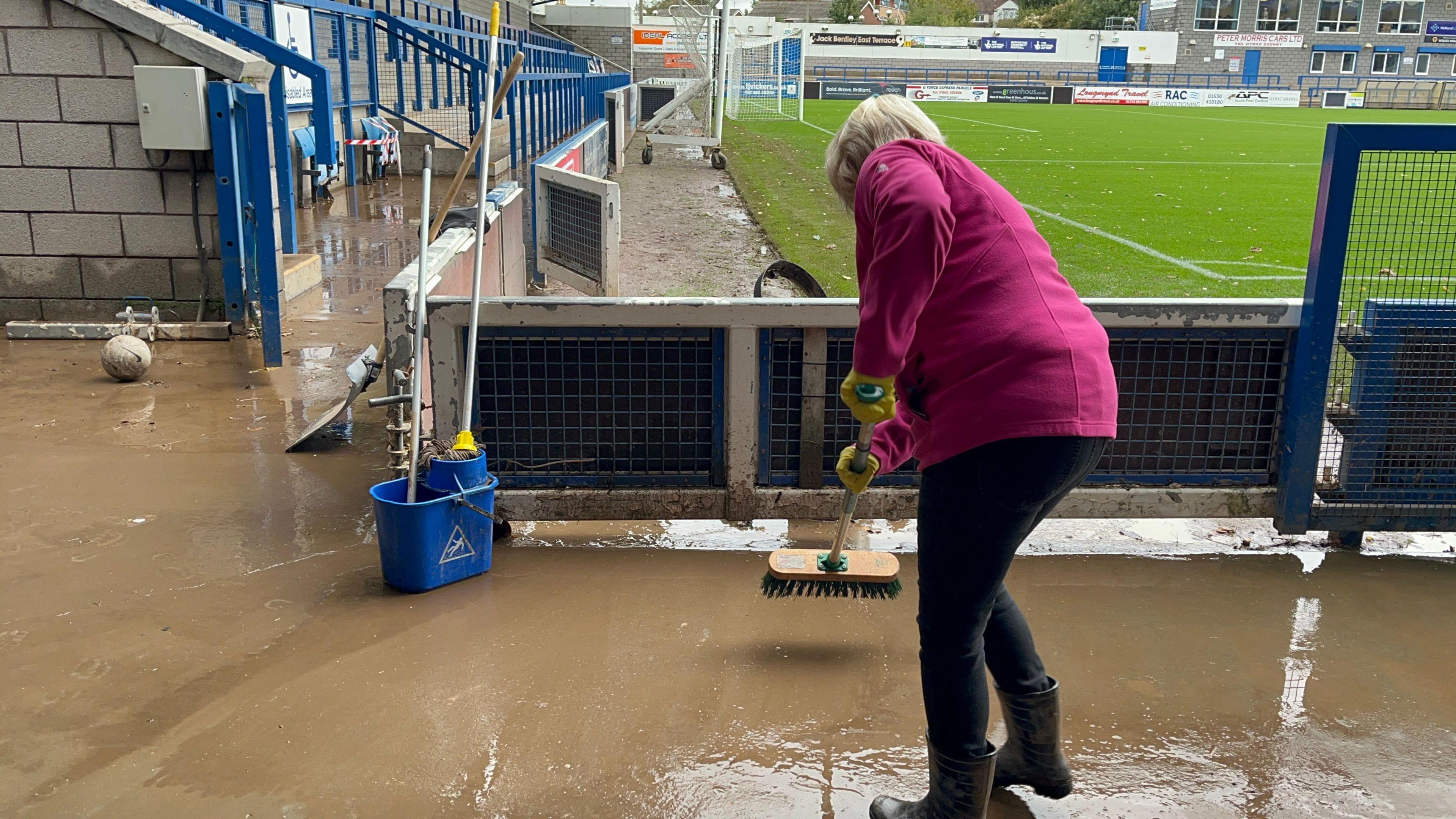 Woman sweeps at water after flooding at AFC Telford stadium