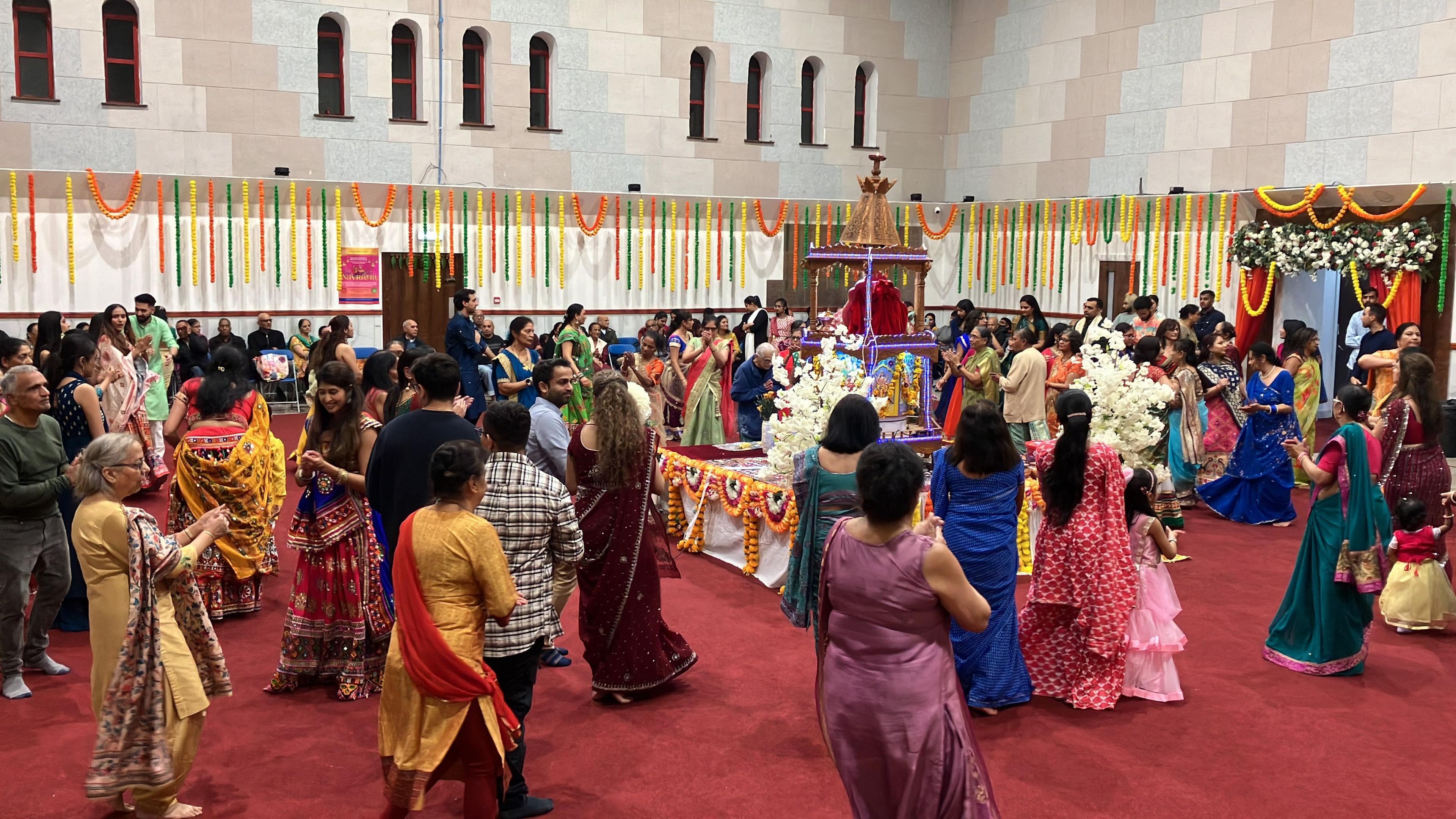 Many people dressed in colourful clothing dancing around a colourful shrine