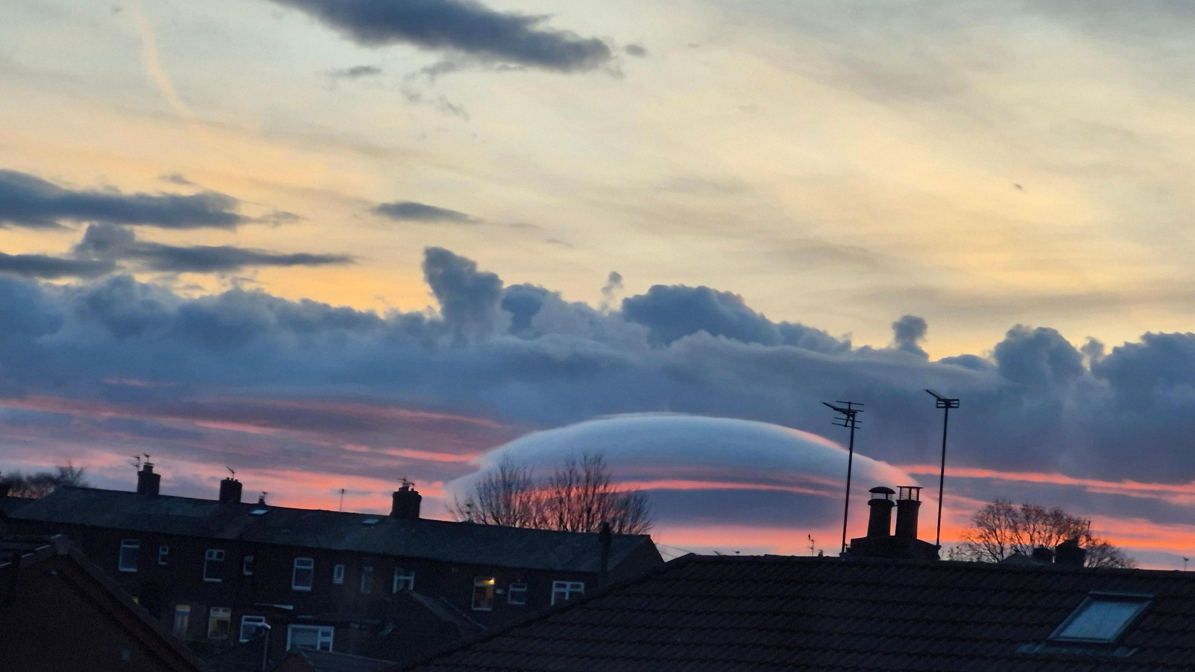 A cloud that resembles a flying saucer can be seen in an orange sky above houses