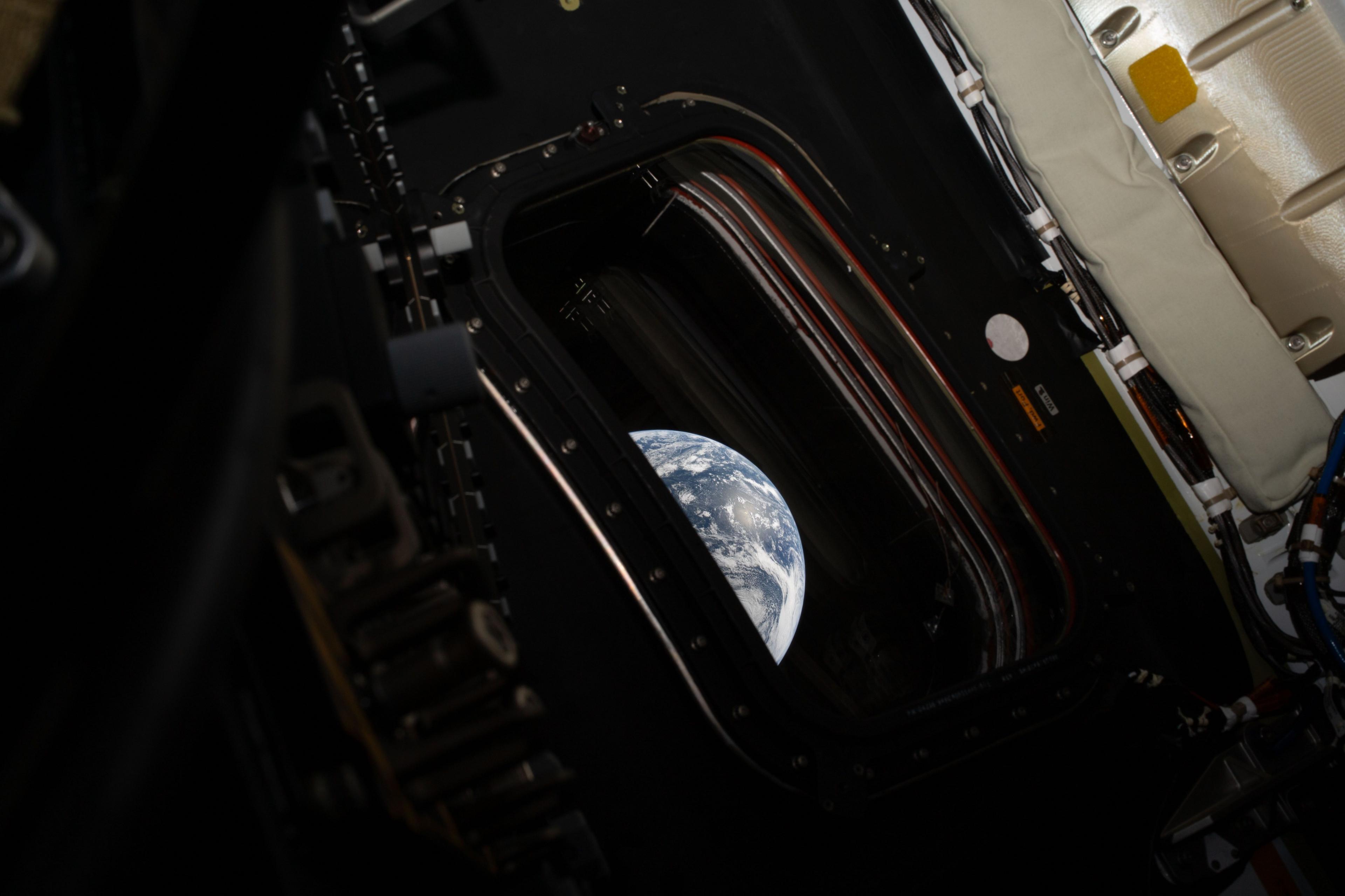 An image from inside of the Orion capsule, which shows a small window and part of the Earth outside