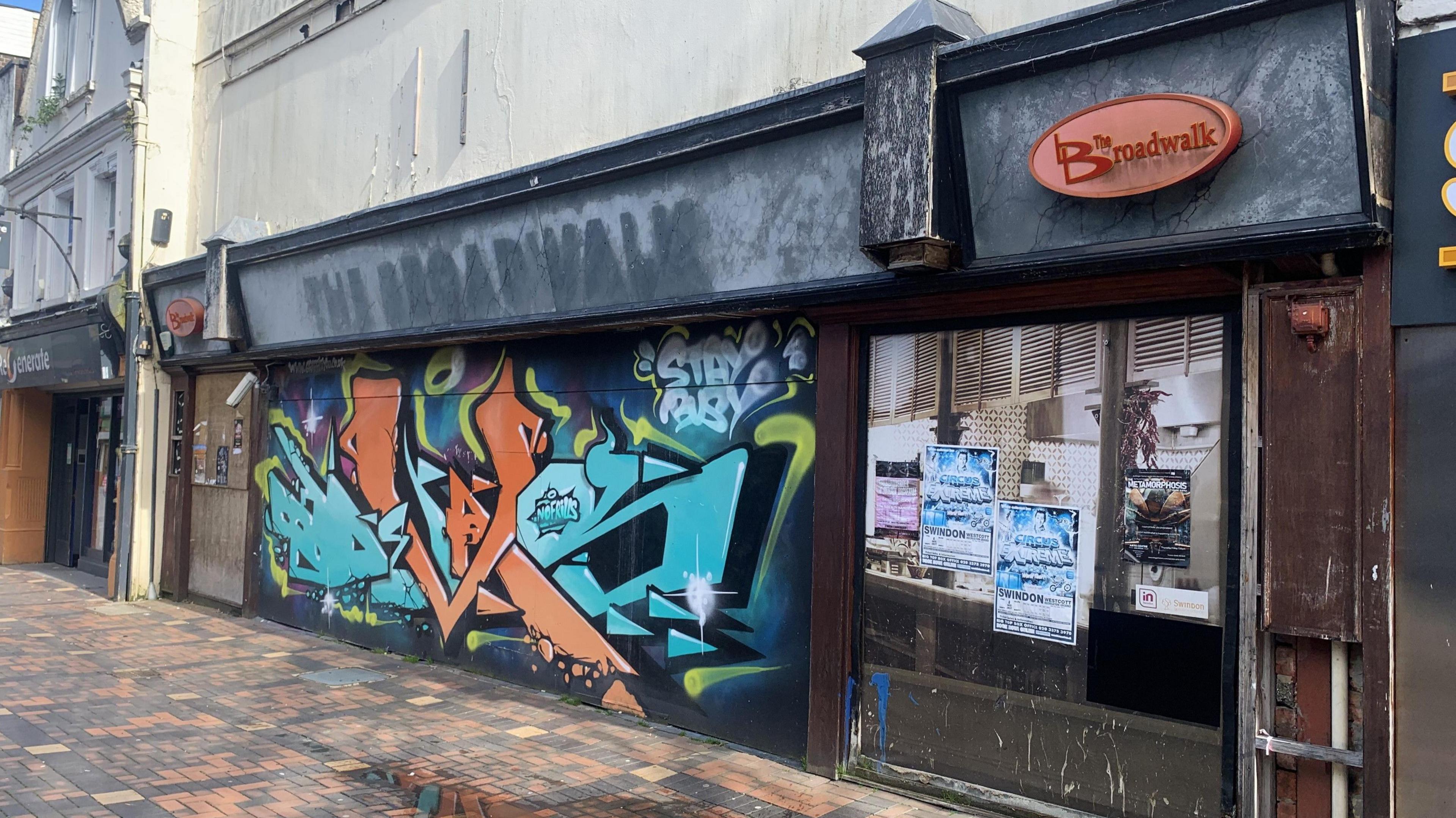 The front of a graffitied and old bar, the lettering pulled off and paint peeling.