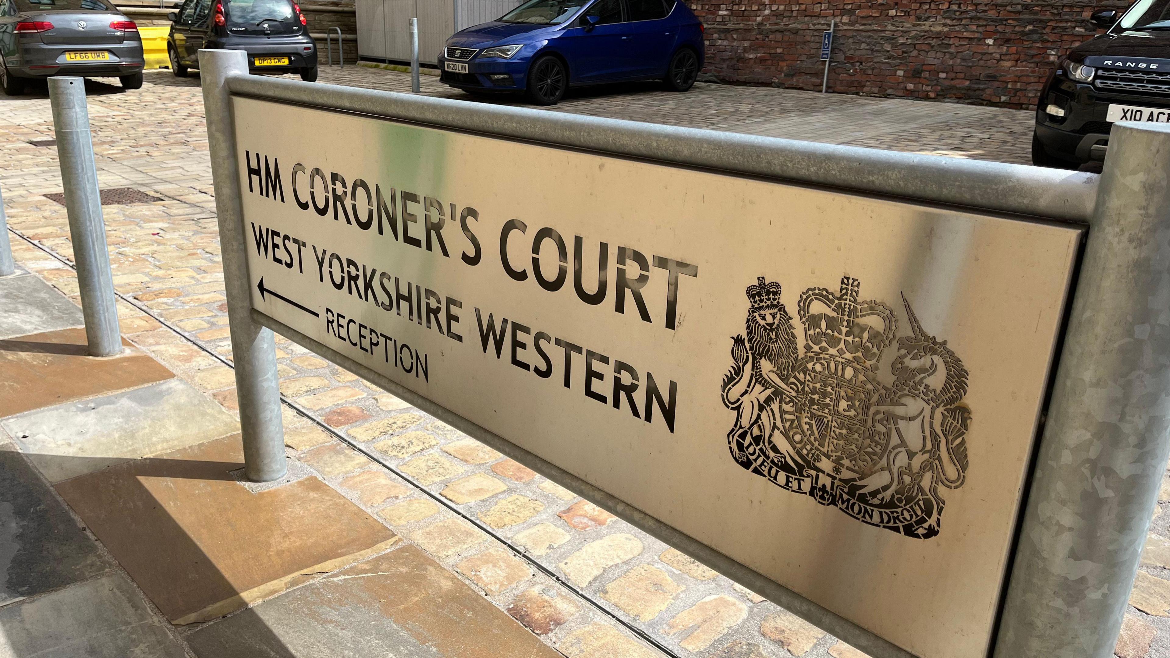 Bradford coroner's court sign, with cars parked in a car park behind it. 