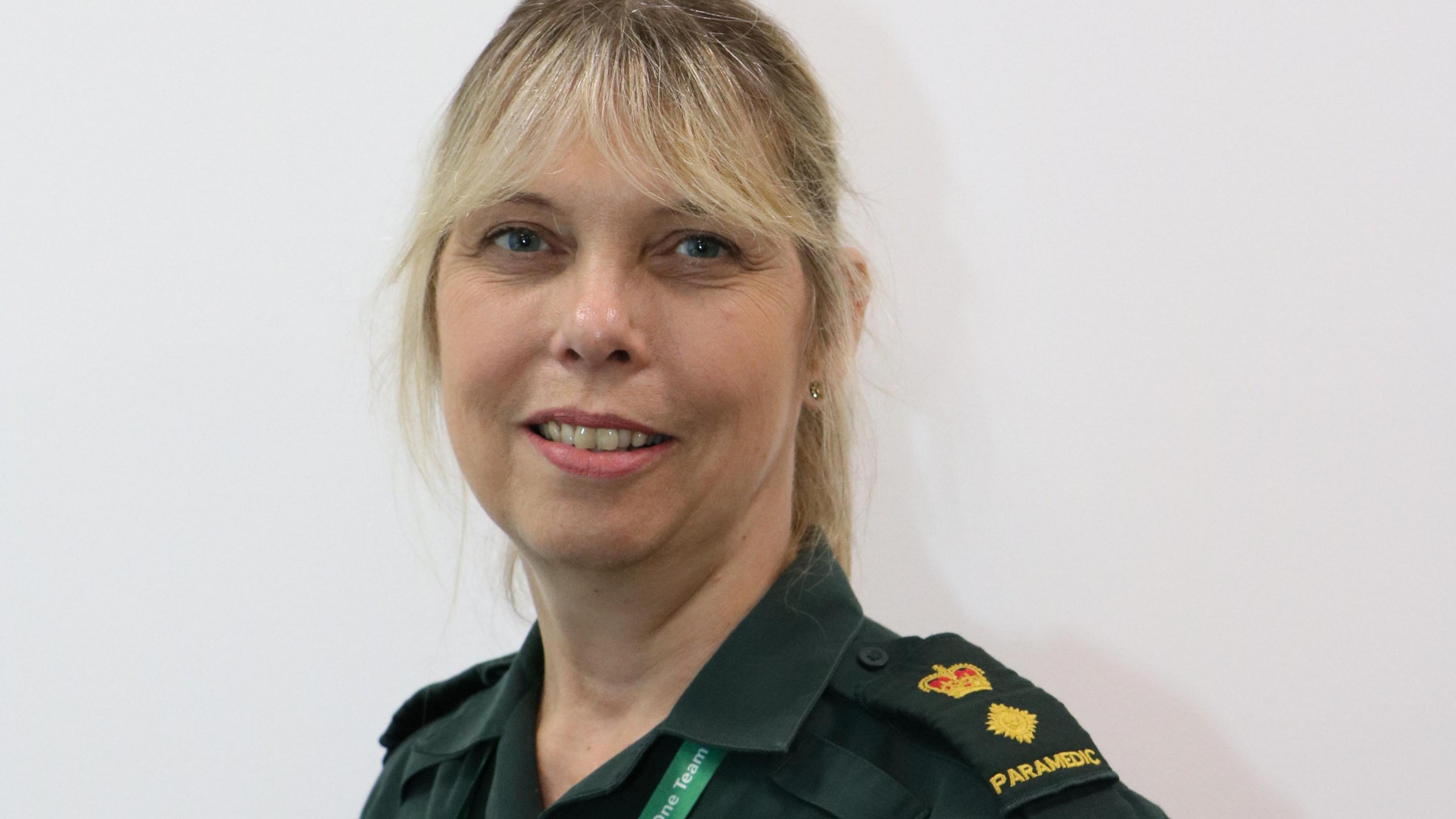 A blonde woman in a green uniform that says 'paramedic' on the shoulder