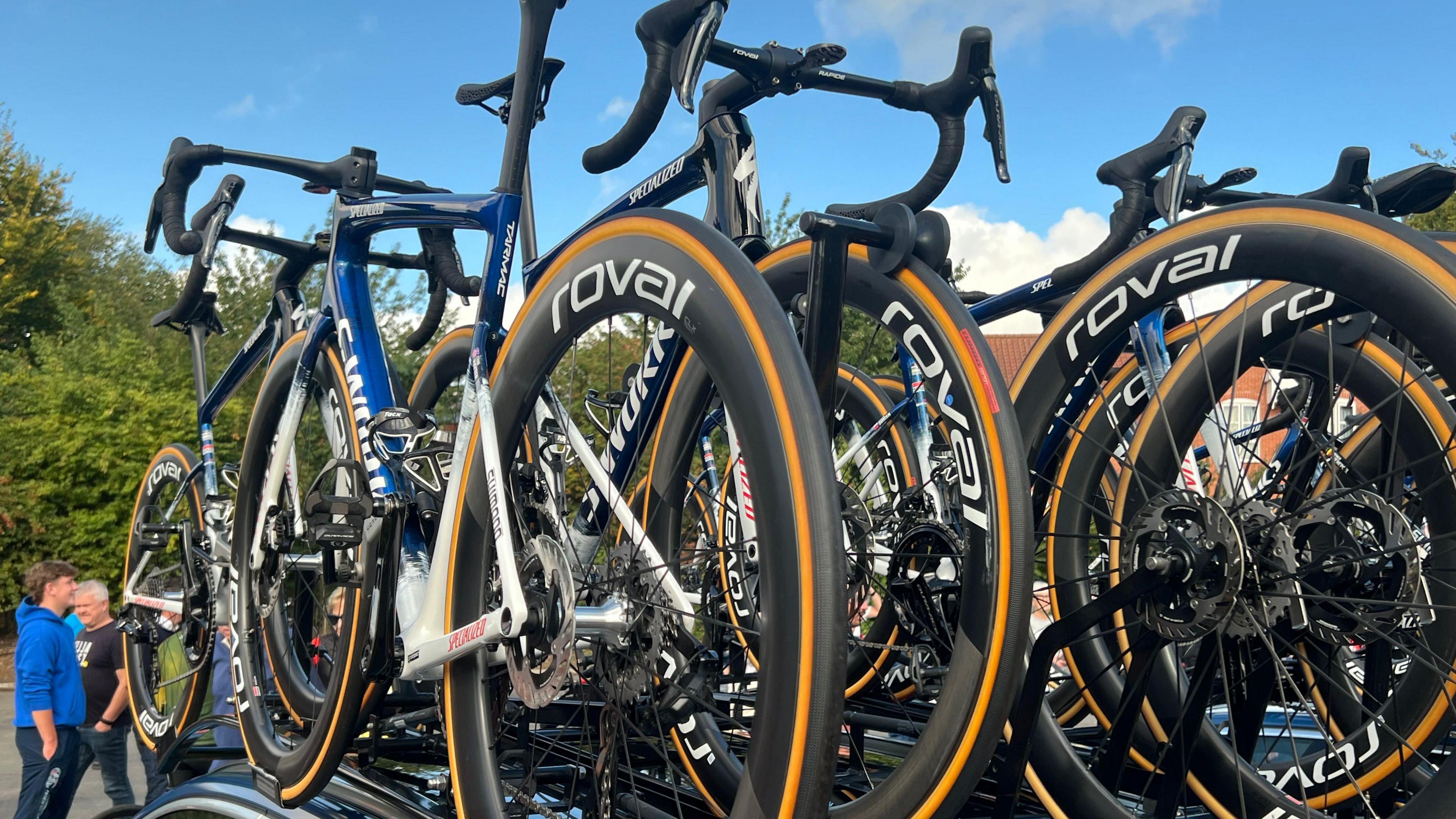A stack of racing bikes rest on top of a car. The bikes are all designed in the same way and are all painted in a blue paint. 