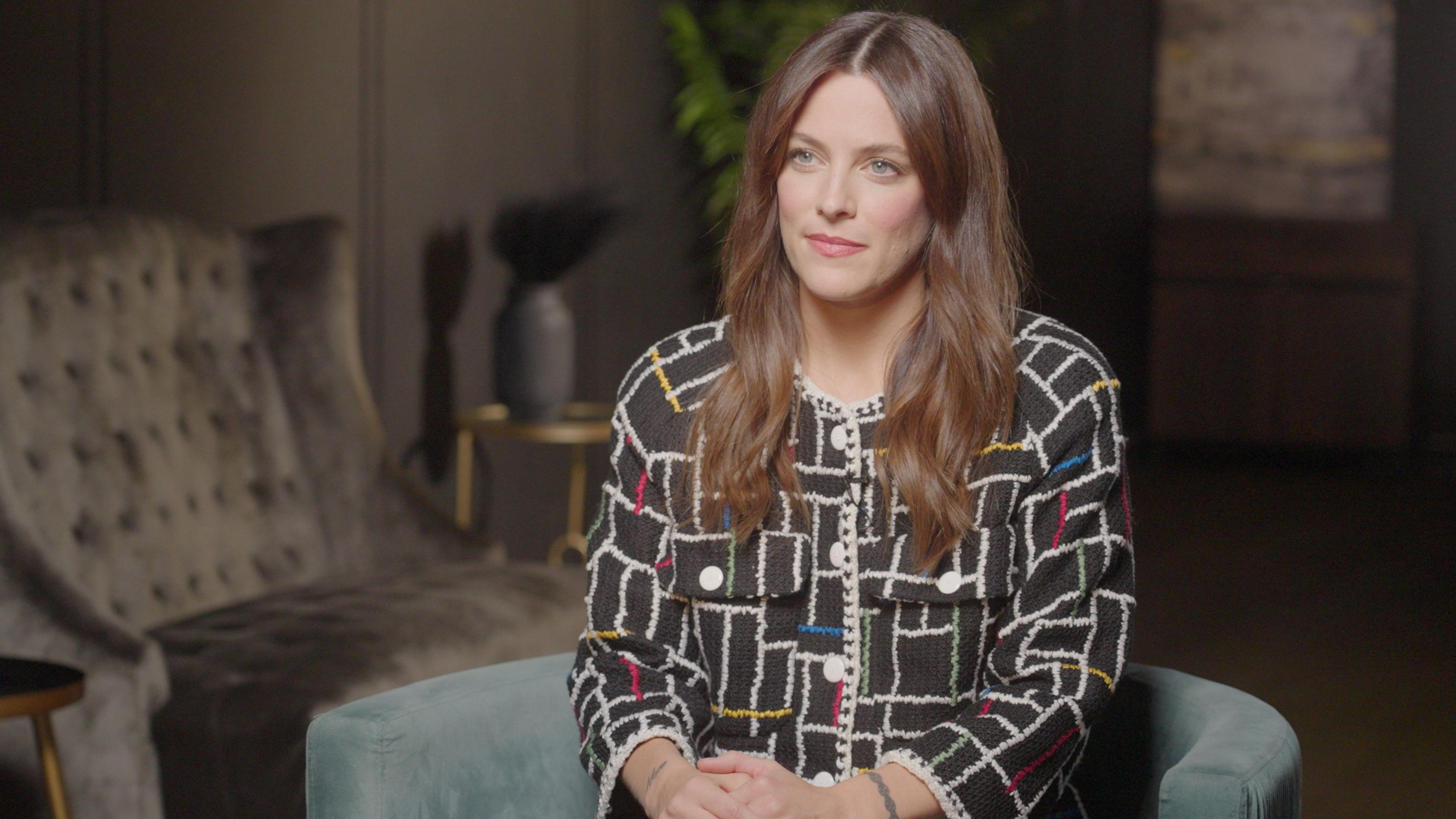 Riley Keough sits smiling for an interview in a living room 