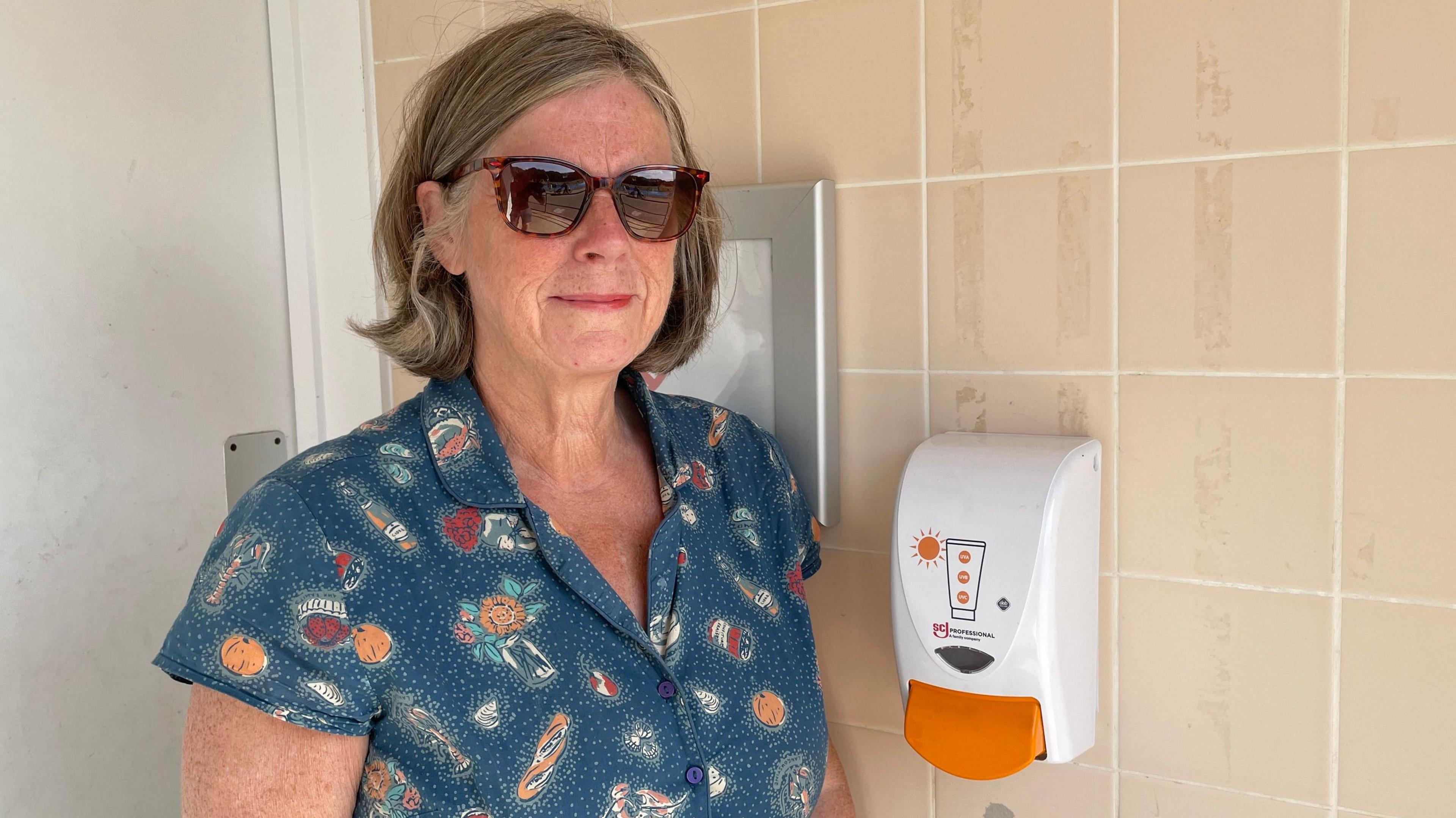 Councillor Lynne Schuller from Bassetlaw District Council standing next to a suncream dispenser at Langold Country Park between Worksop and Rotherham. She is wearing a blue dress and sunglasses.