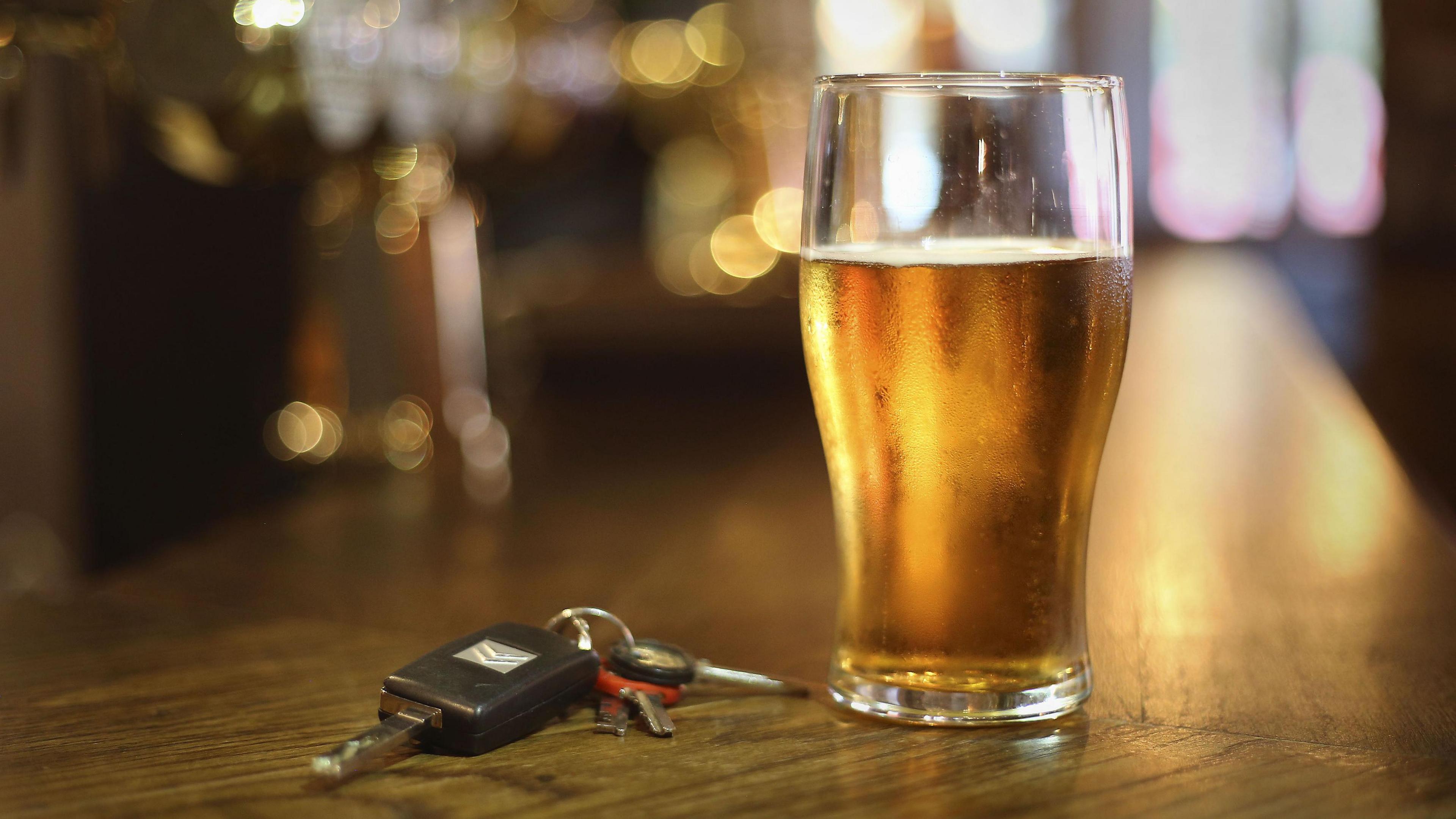 A pint of beer on a bar with keys next to it.