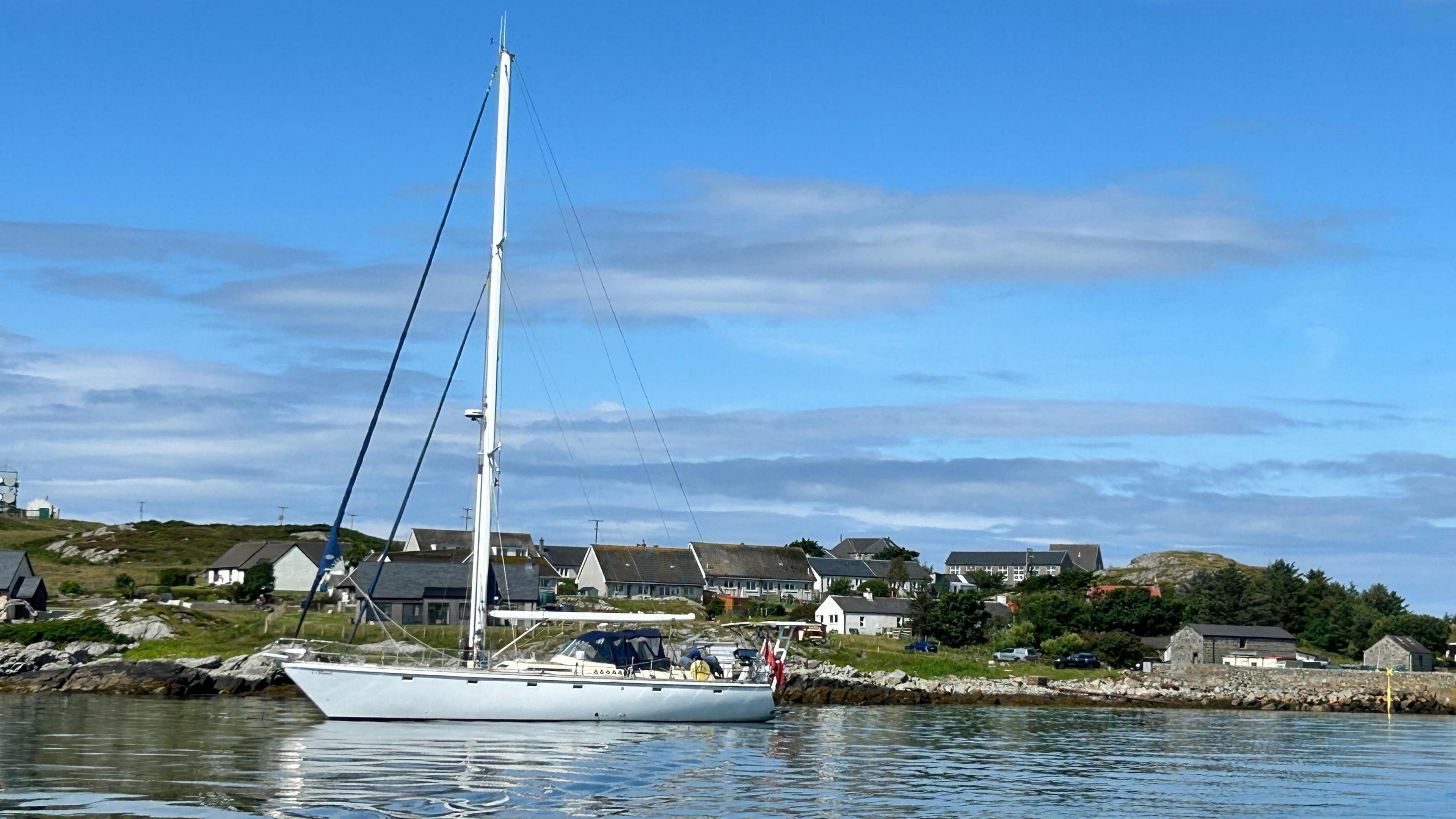 An exterior view of a white yacht, floating on the water with some houses behind it