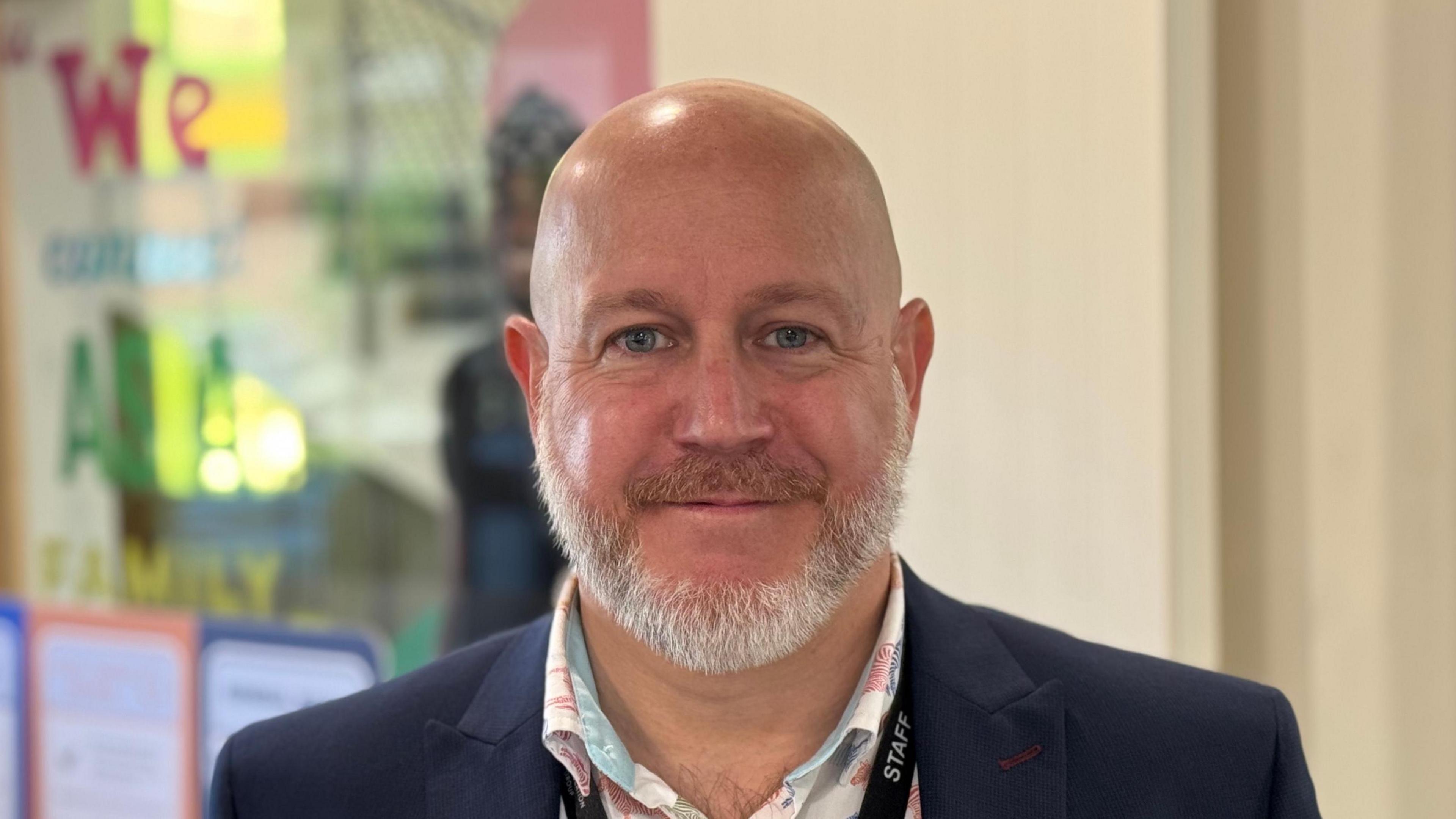 A head shot of Phil Stittle. He has white facial hair and is wearing a blazer over a shirt. He is smiling into the camera.